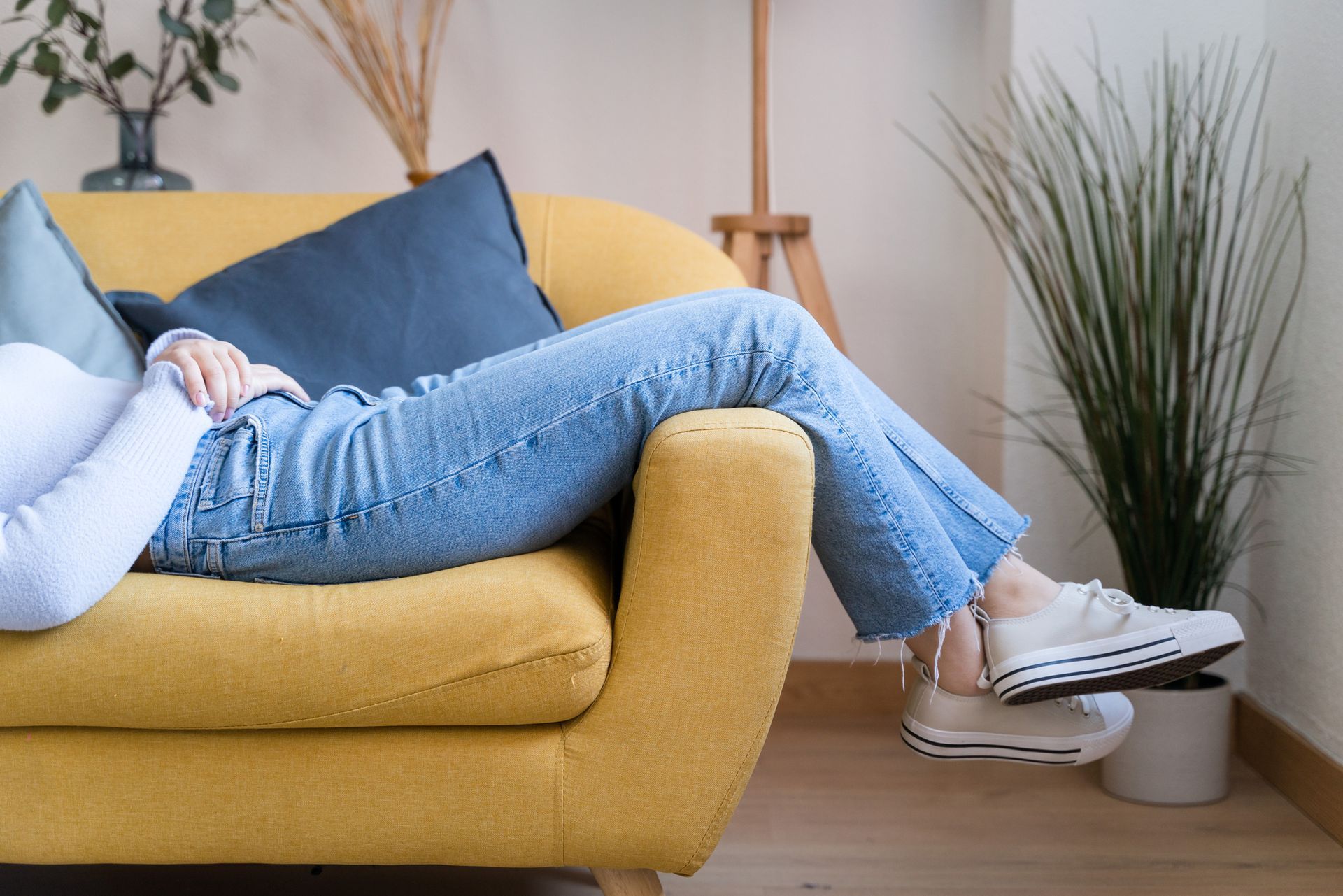 A woman is laying on a yellow couch with her legs crossed.