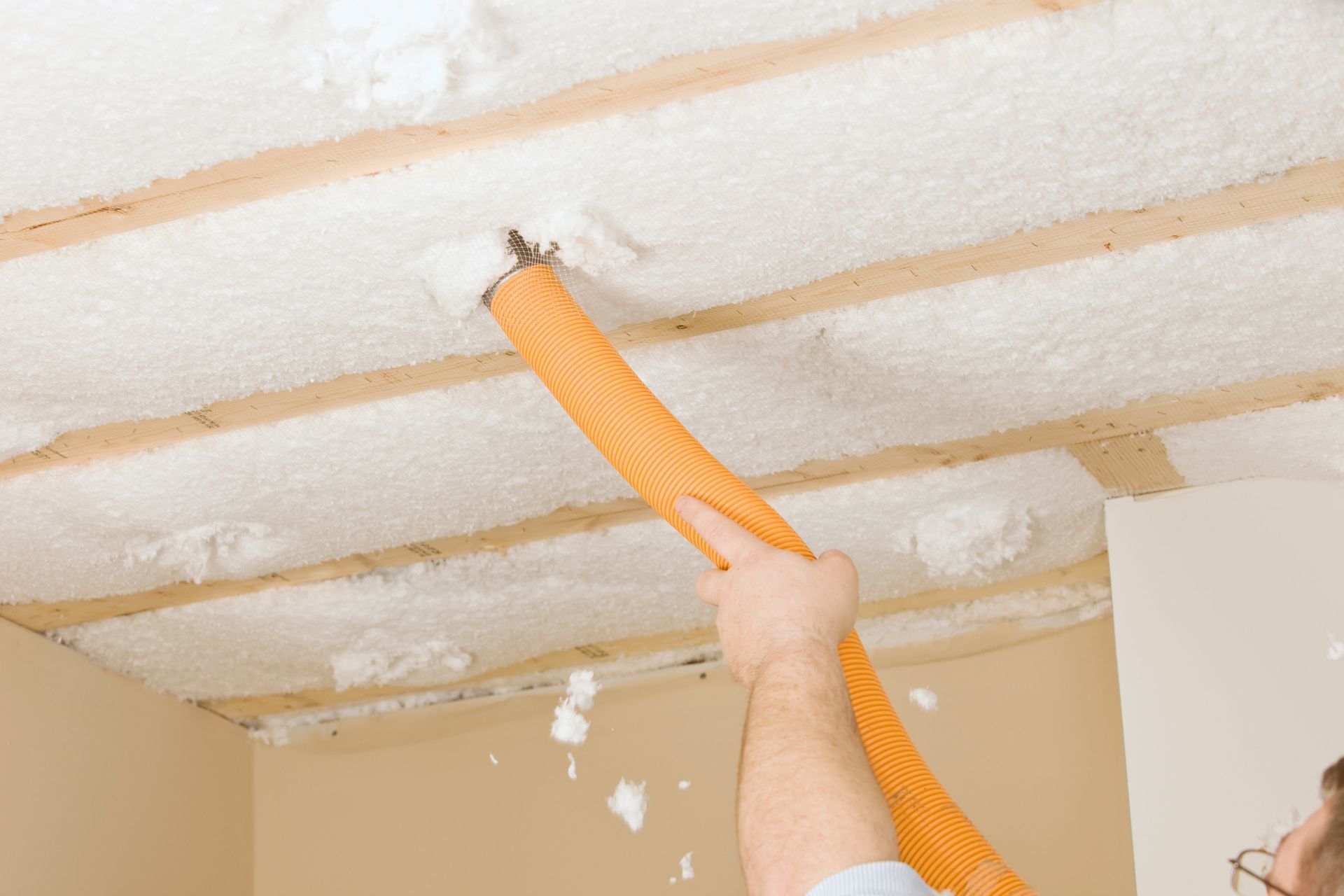 A man is blowing foam from the ceiling with a vacuum cleaner.