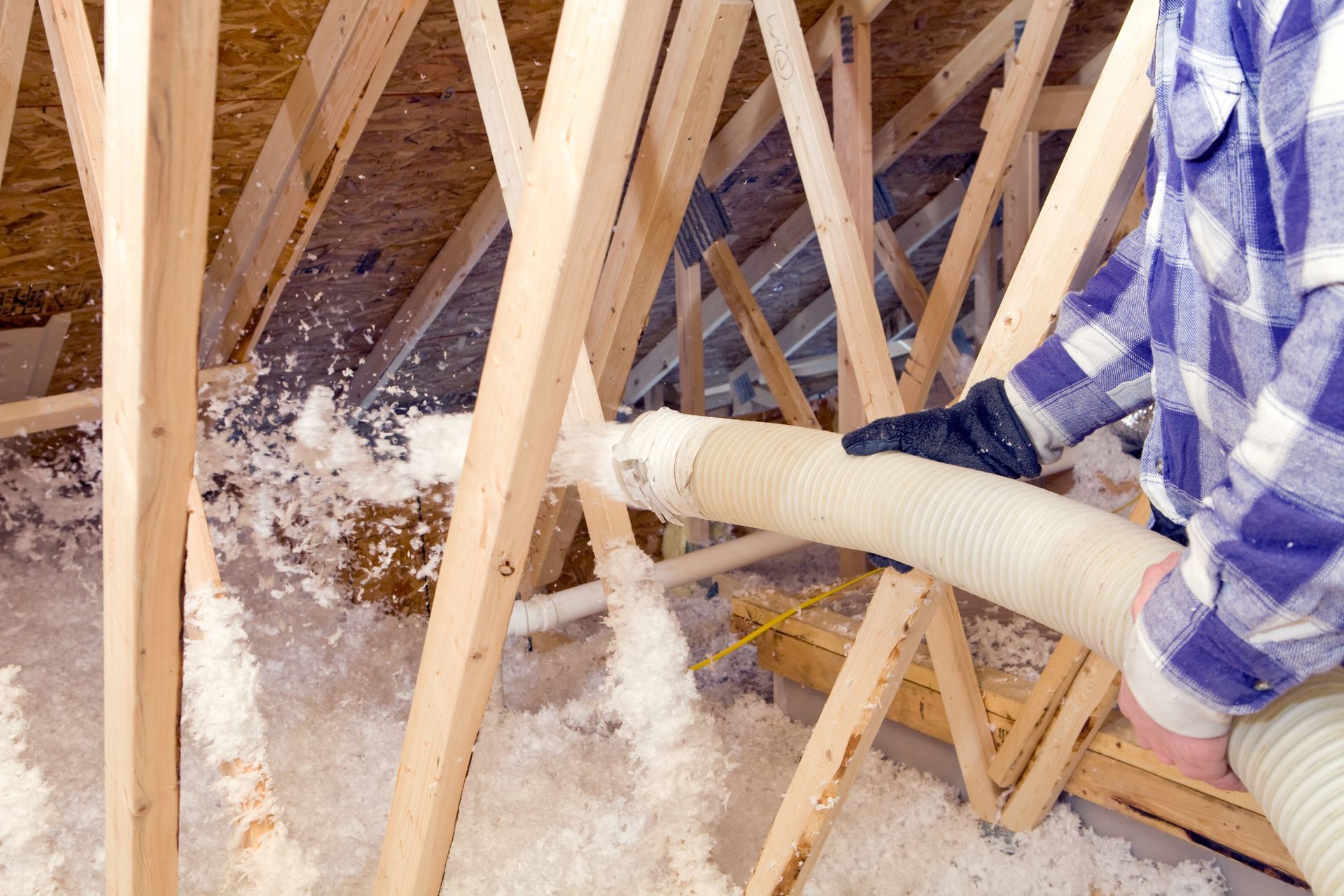 A person is blowing insulation into the attic of a house.