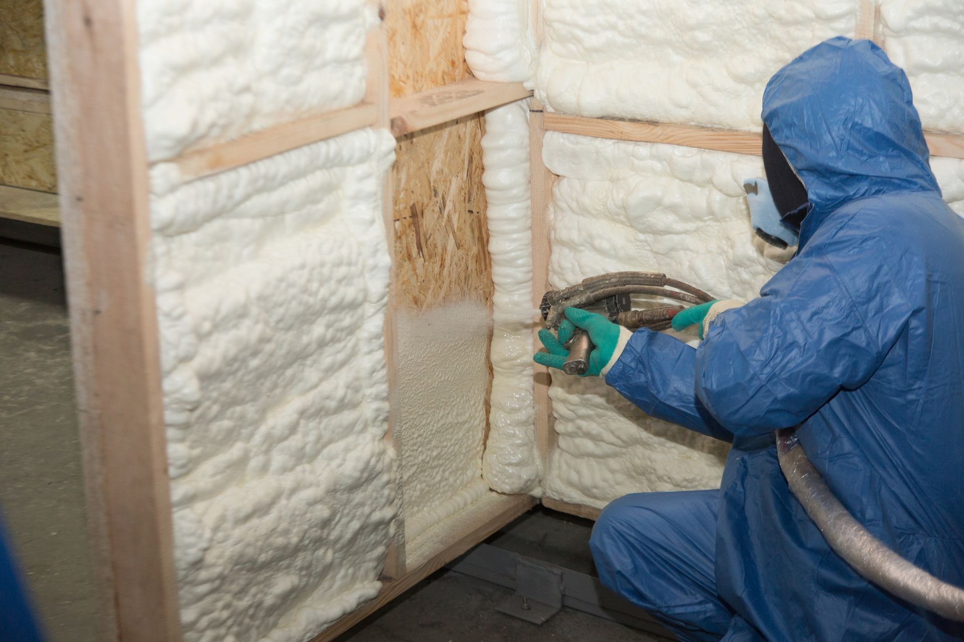 A man in a blue suit is spraying foam on a wall.