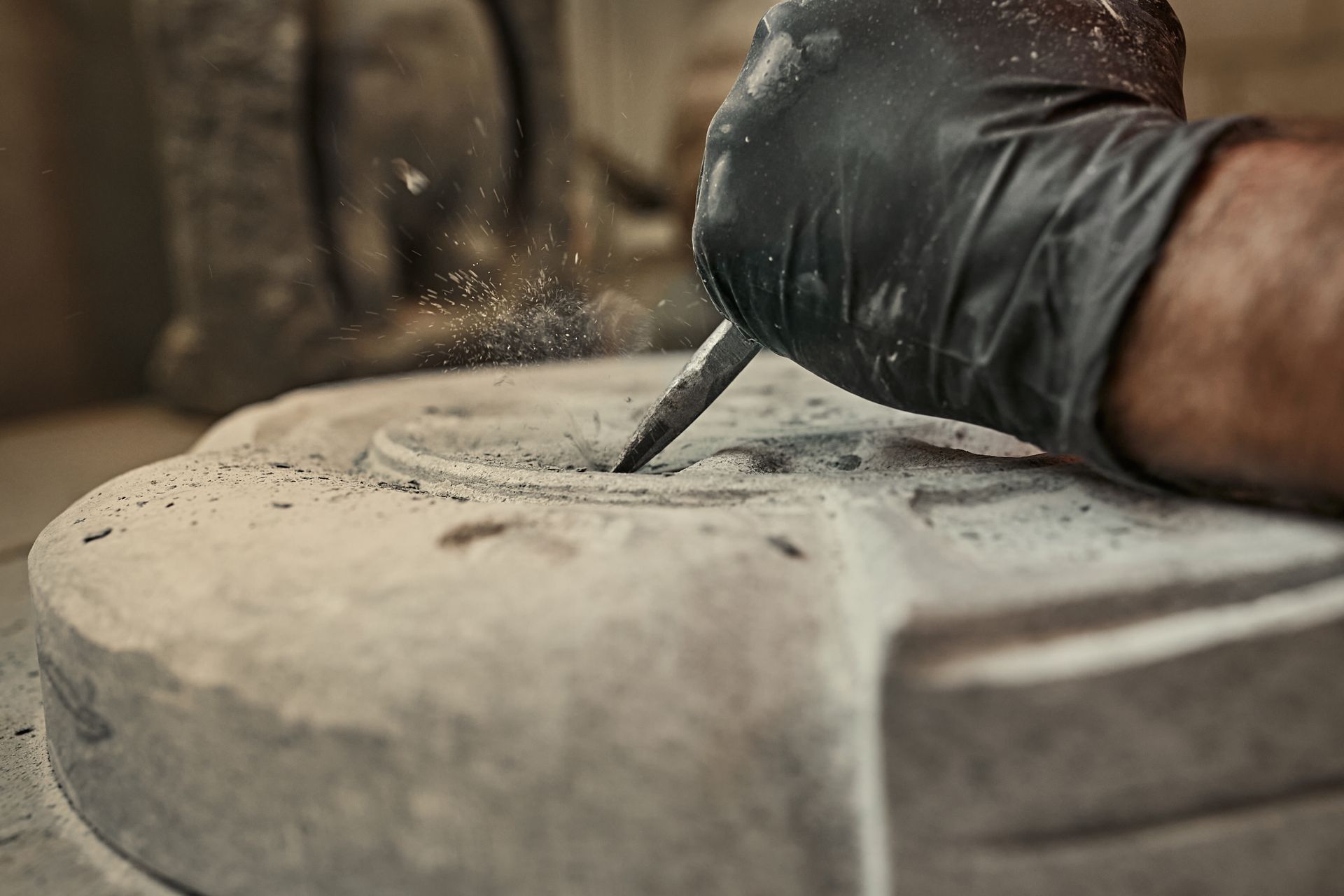 Gloved hand carving a stone surface with a chisel, close-up in a workshop