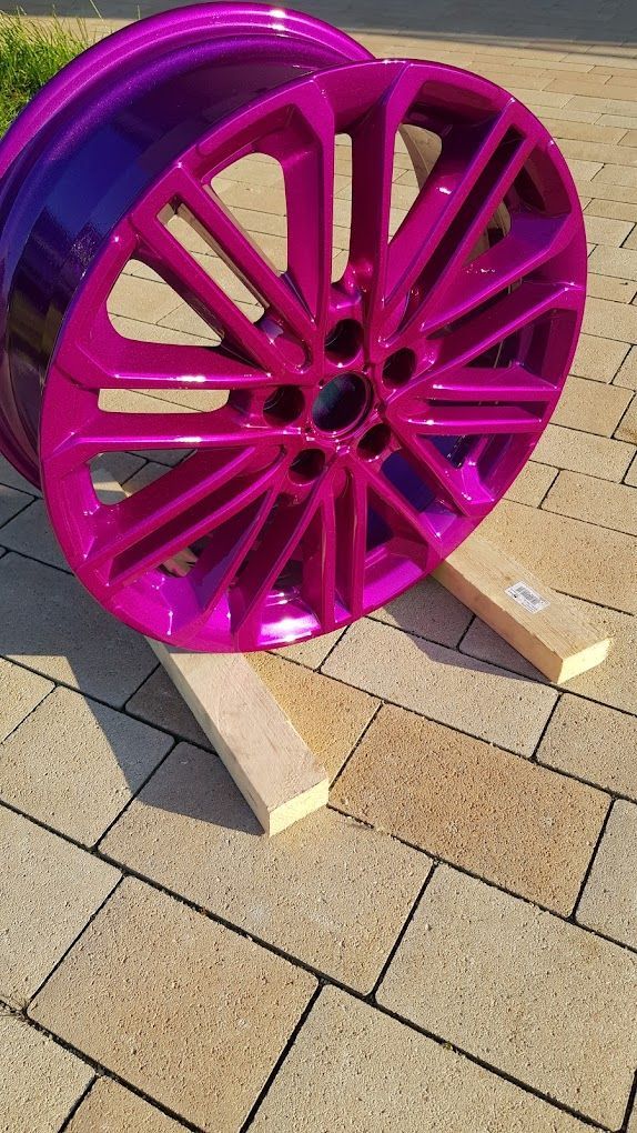 Eine rosa Felge steht auf einem Holzständer auf einem gepflasterten Gehweg.