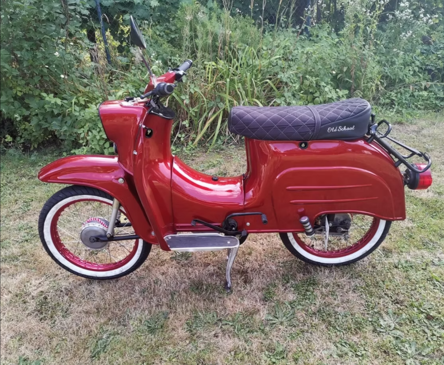 Ein roter Motorroller mit weißen Reifen steht im Gras.
