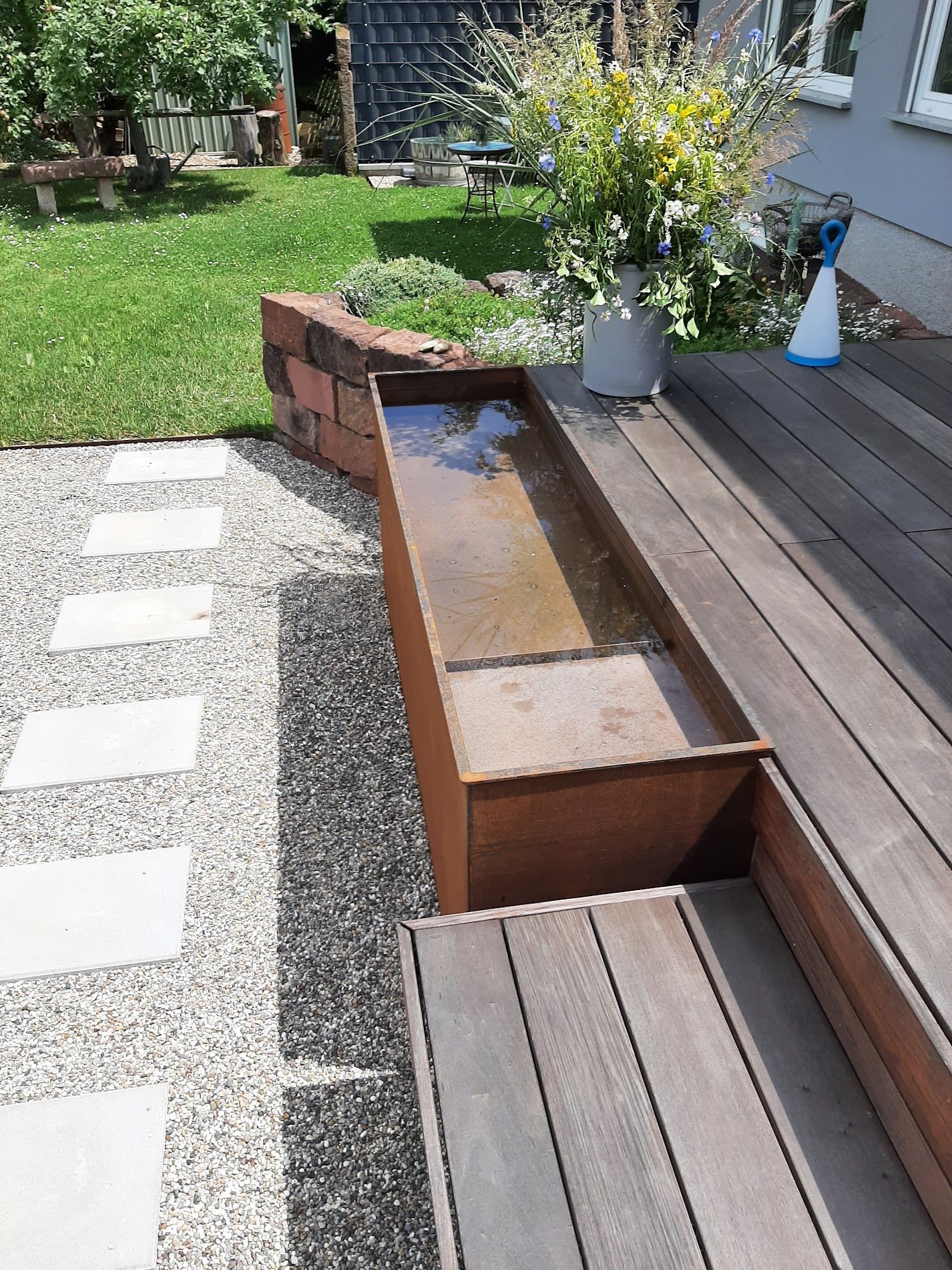 Ein Holzdeck mit einem Blumentopf und einer Sprühflasche darauf.