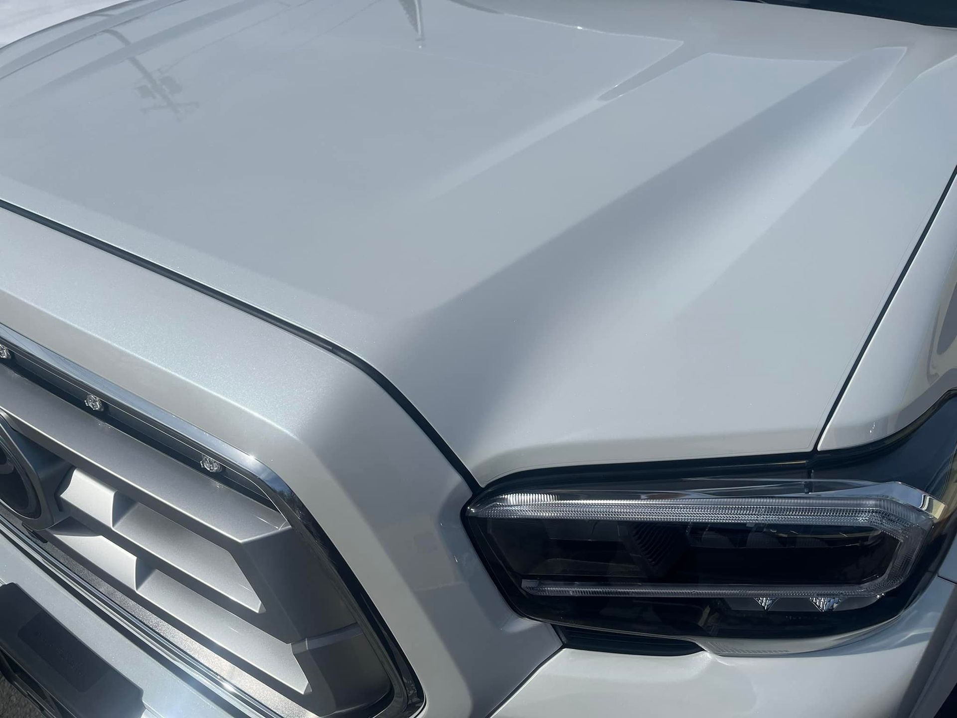 Close-up view of the front hood, grille, and passenger-side headlight of a white pickup truck.