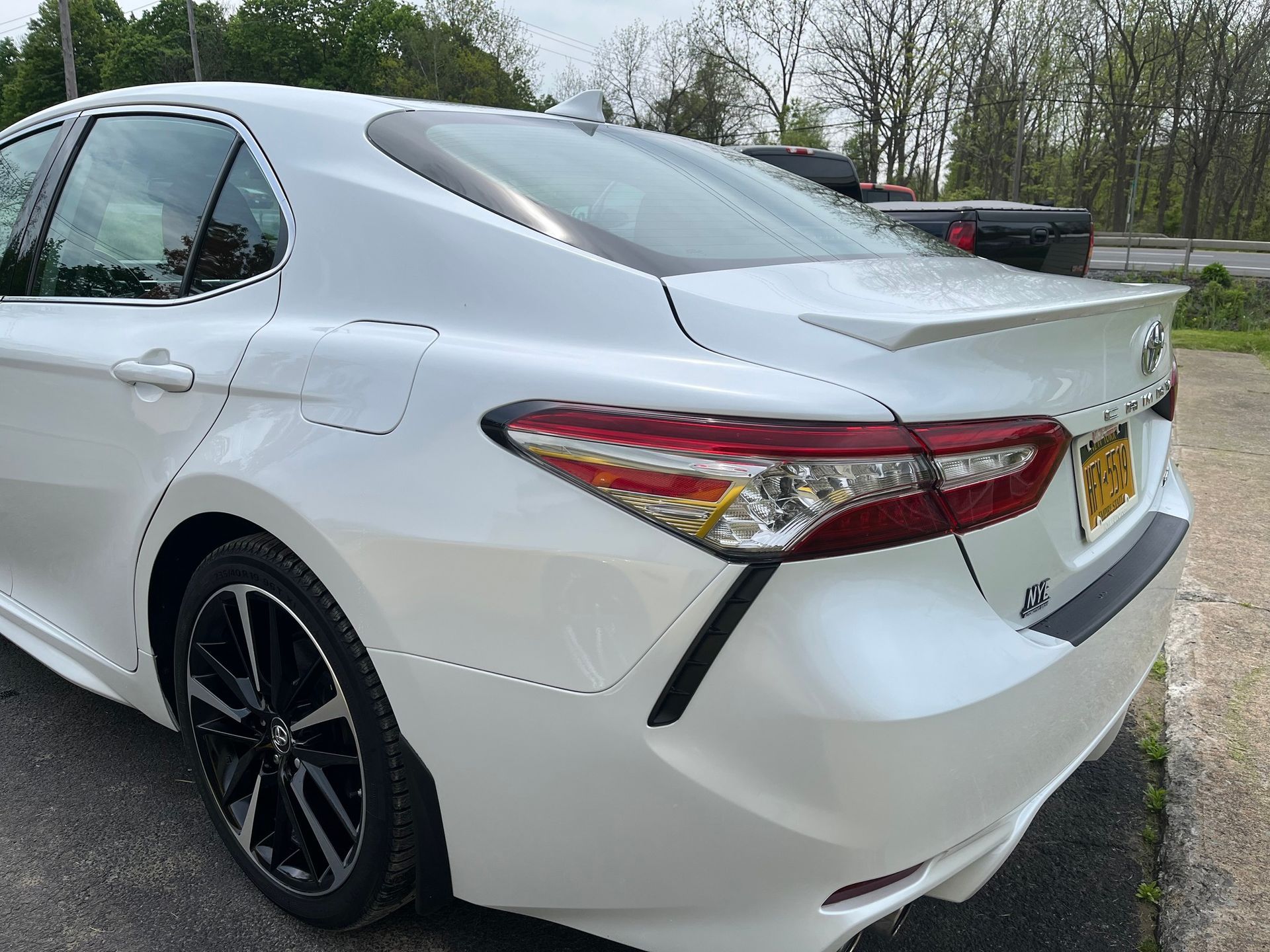 A white Toyota Camry sedan parked on asphalt, shown from a rear three-quarter angle.