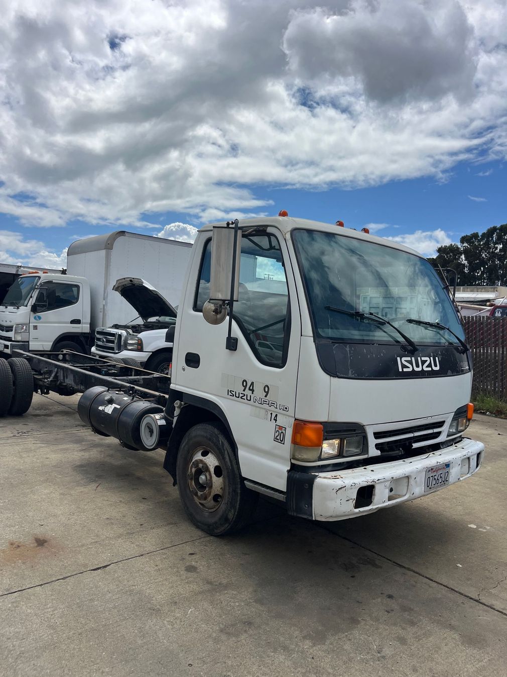 Mechanic in blue overalls and cap working on a truck engine, reaching with a gloved hand.