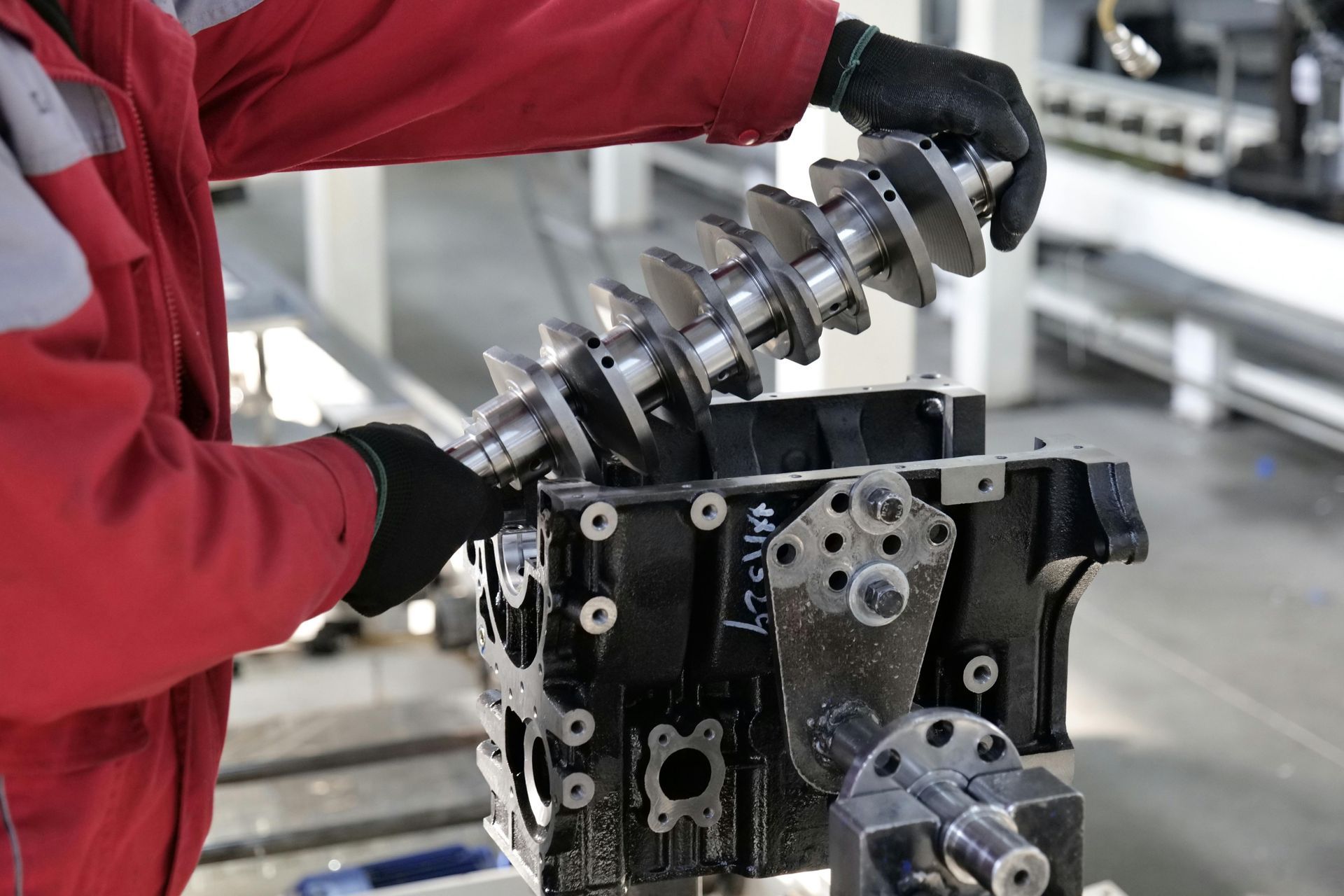Mechanic assembling engine components in a workshop; black gloves, red overall.