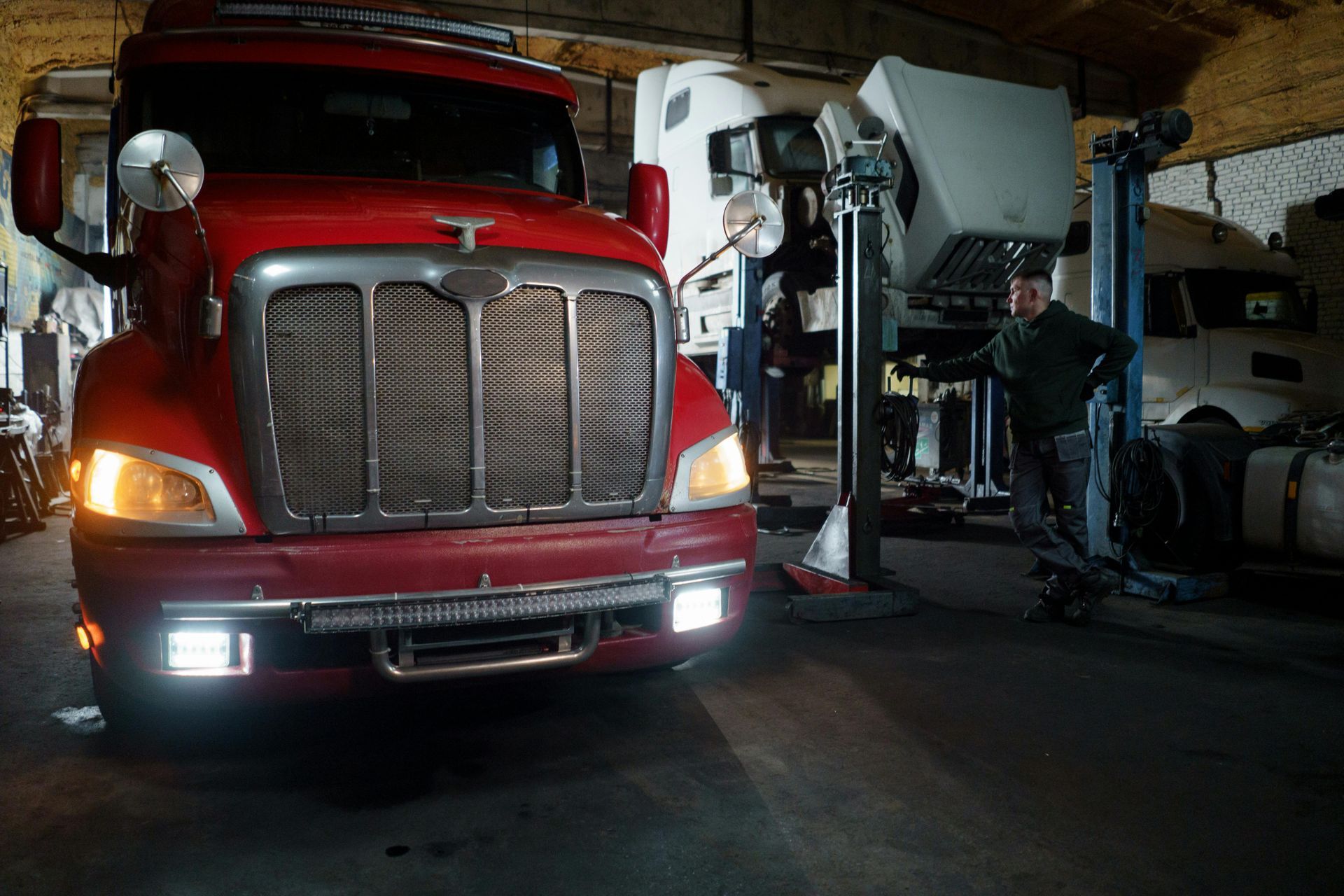 Red semi-truck in a dimly lit garage; a person stands near a lift.