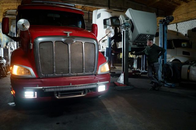 Red semi-truck in a dimly lit garage; a person stands near a lift.