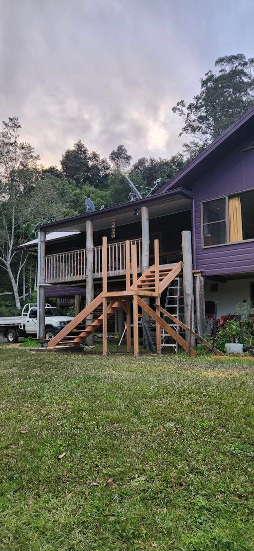 A House With a Wooden Deck is Sitting on Top of a Lush Green Field — Mark Cannon Carpentry & Maintenance in Moonee Beach, NSW