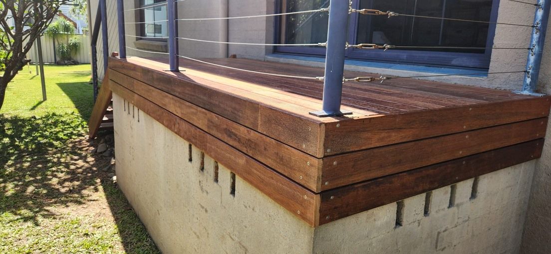 A Wooden Deck With a Metal Railing is Sitting on a Concrete Base — Mark Cannon Carpentry & Maintenance in Moonee Beach, NSW