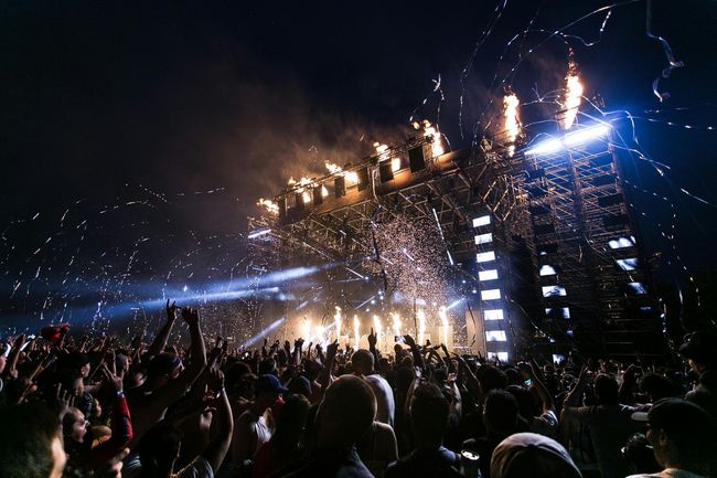 Concert crowd with stage, pyrotechnics, and confetti at night.