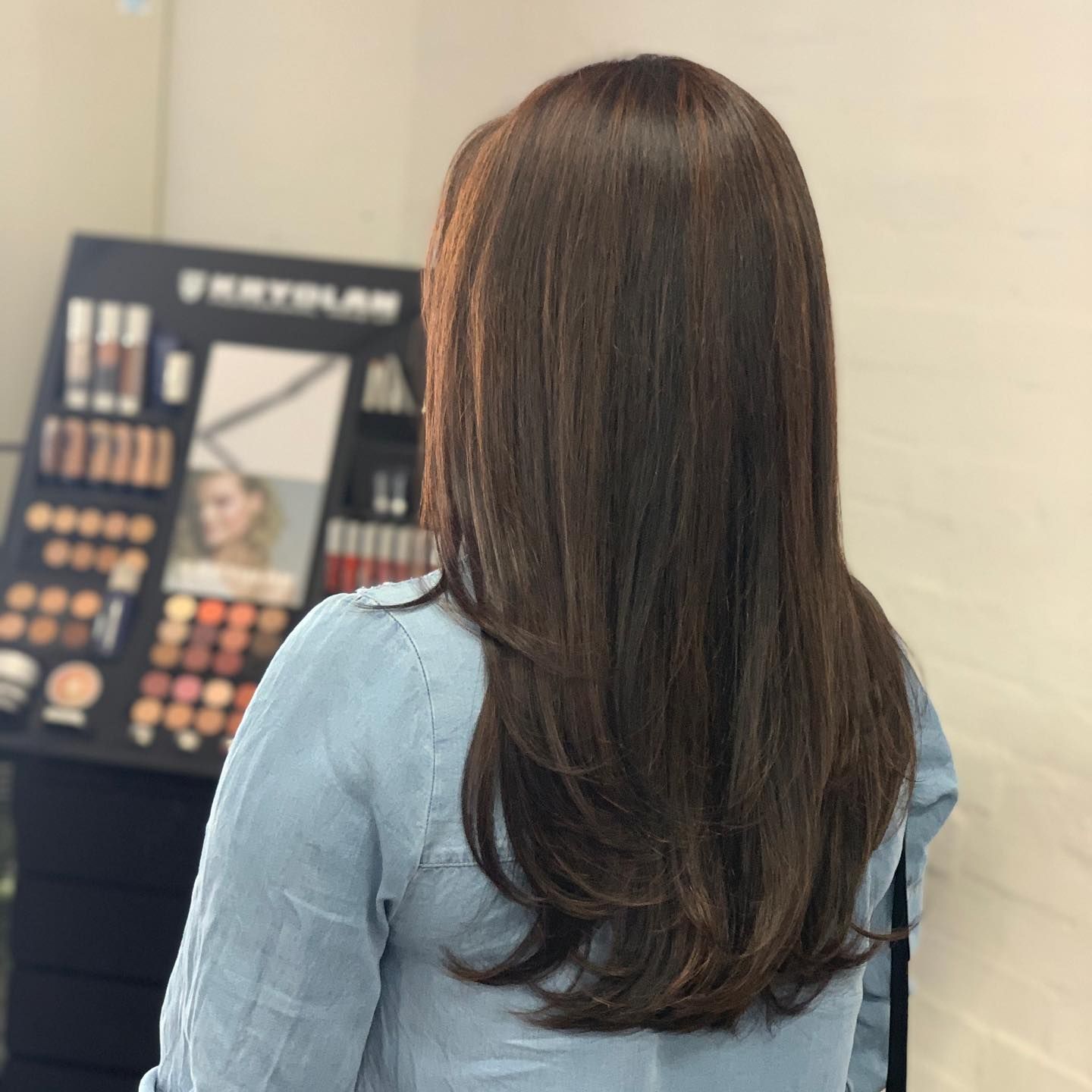 Woman With Long, Layered Brown Hair in a Beauty Salon, Looking at a Makeup Display — Lavish Hair in Shepparton, VIC