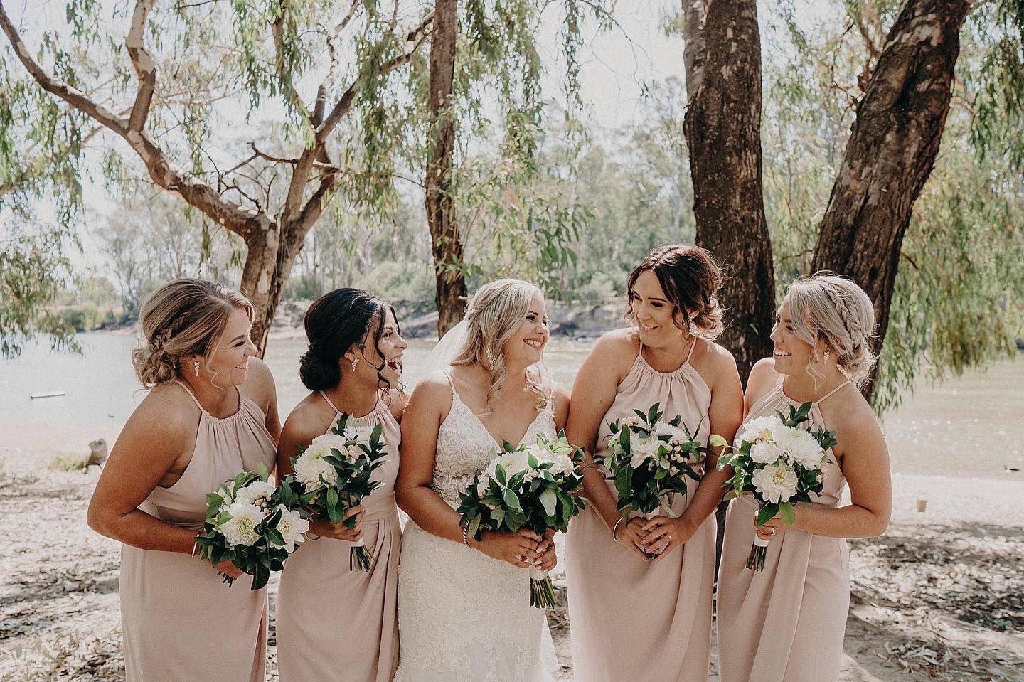 Bride and Bridesmaids in Nude Dresses Laugh Outdoors, Holding Bouquets — Lavish Hair in Shepparton, VIC