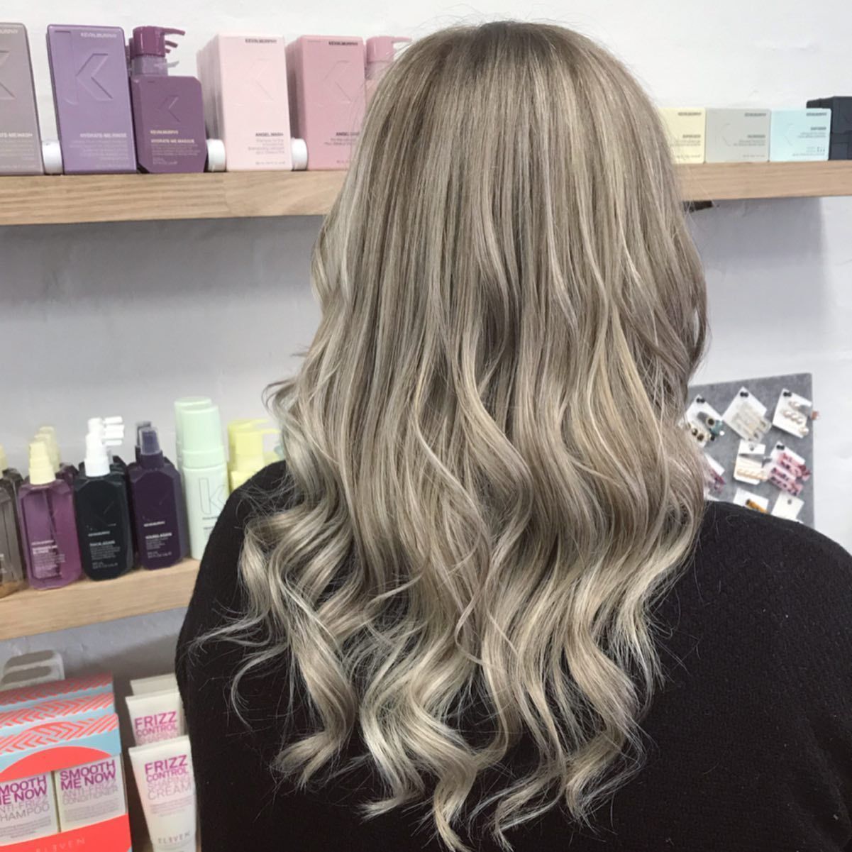 Woman With Wavy Blonde Hair, Standing in Front of a Salon Shelf — Lavish Hair in Shepparton, VIC
