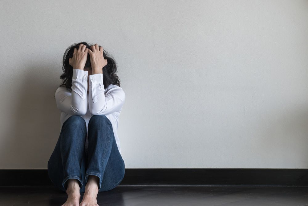 A Woman Is Sitting On The Floor Covering Her Face With Her Hands — Wegner Therapies In Pialba, QLD