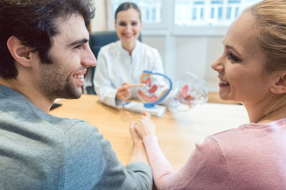 A Man And A Woman Are Sitting At A Table Talking To A Doctor — Wegner Therapies In Pialba, QLD