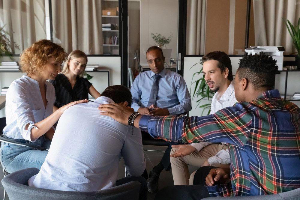 A Group Of People Are Sitting In A Circle With Their Hands On Each Other — Wegner Therapies In Pialba, QLD