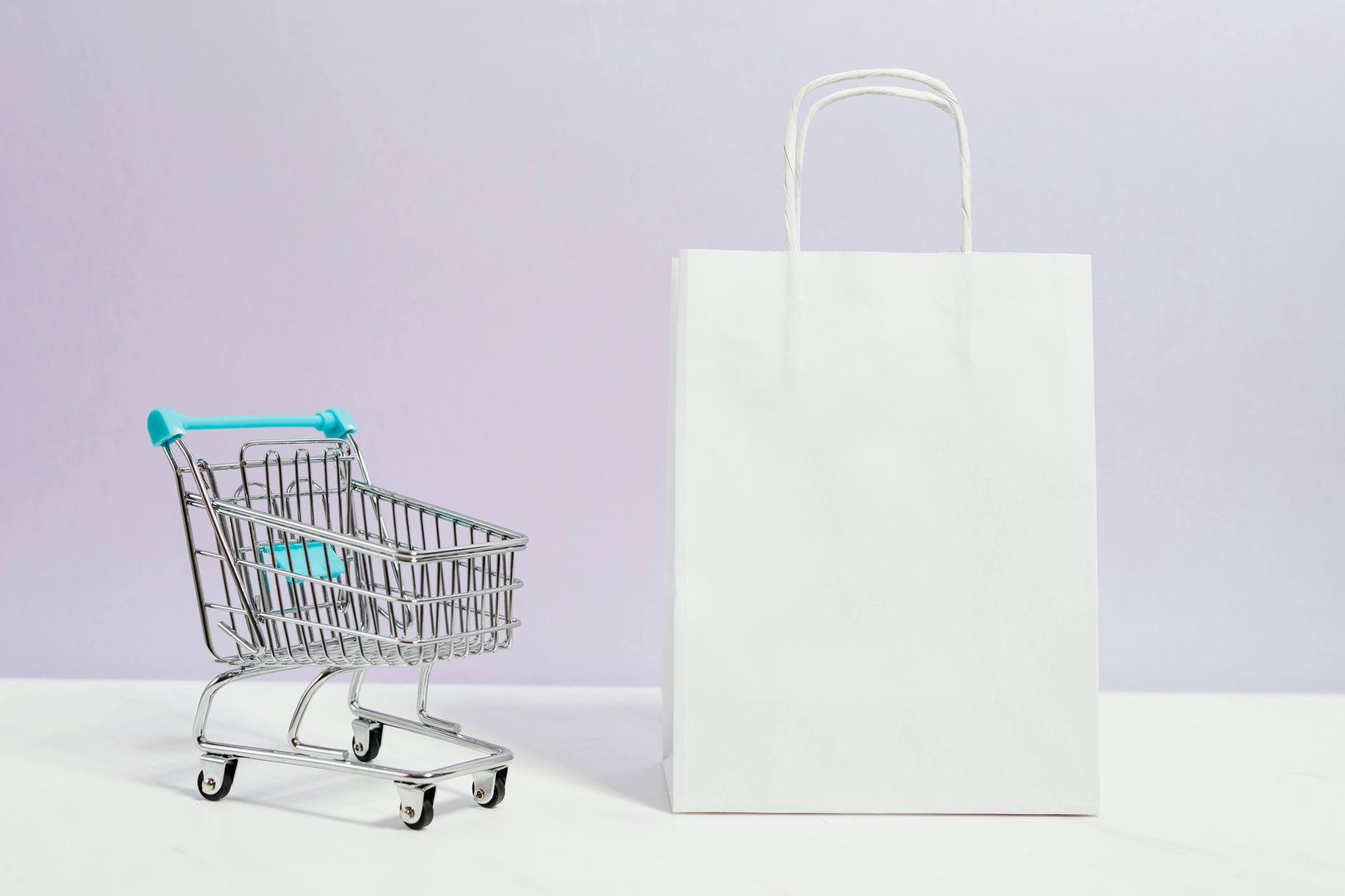 Mini shopping cart next to a white paper bag on a white surface, purple background.