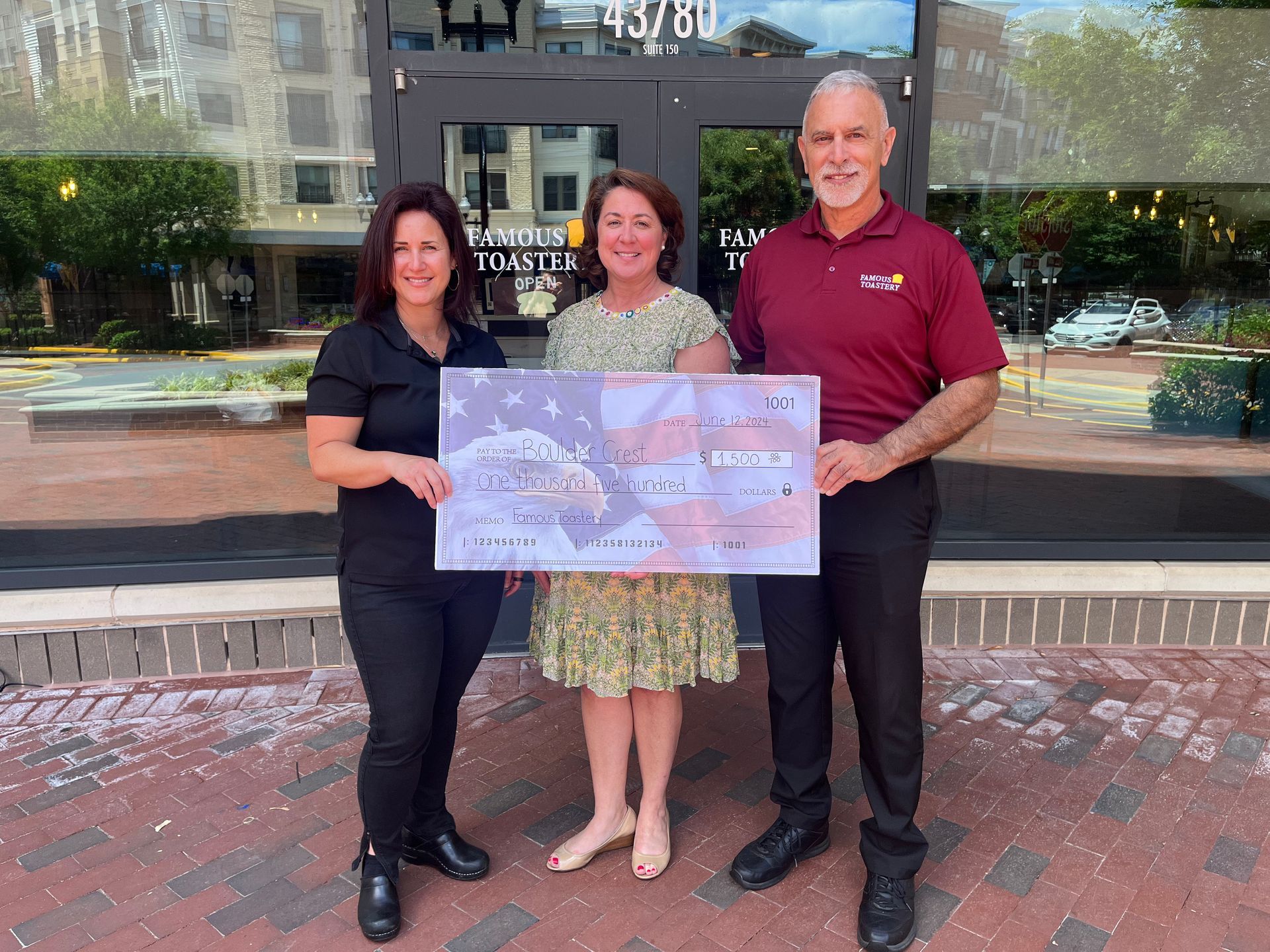 Three people are holding a large check in front of a building.