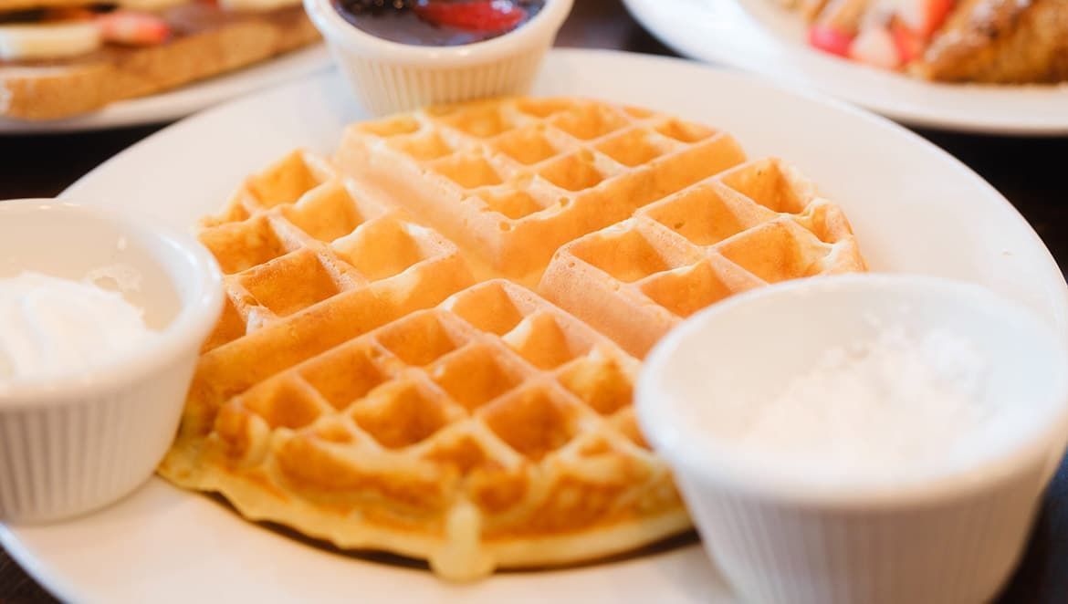 A close up of a waffle on a plate with syrup and whipped cream.