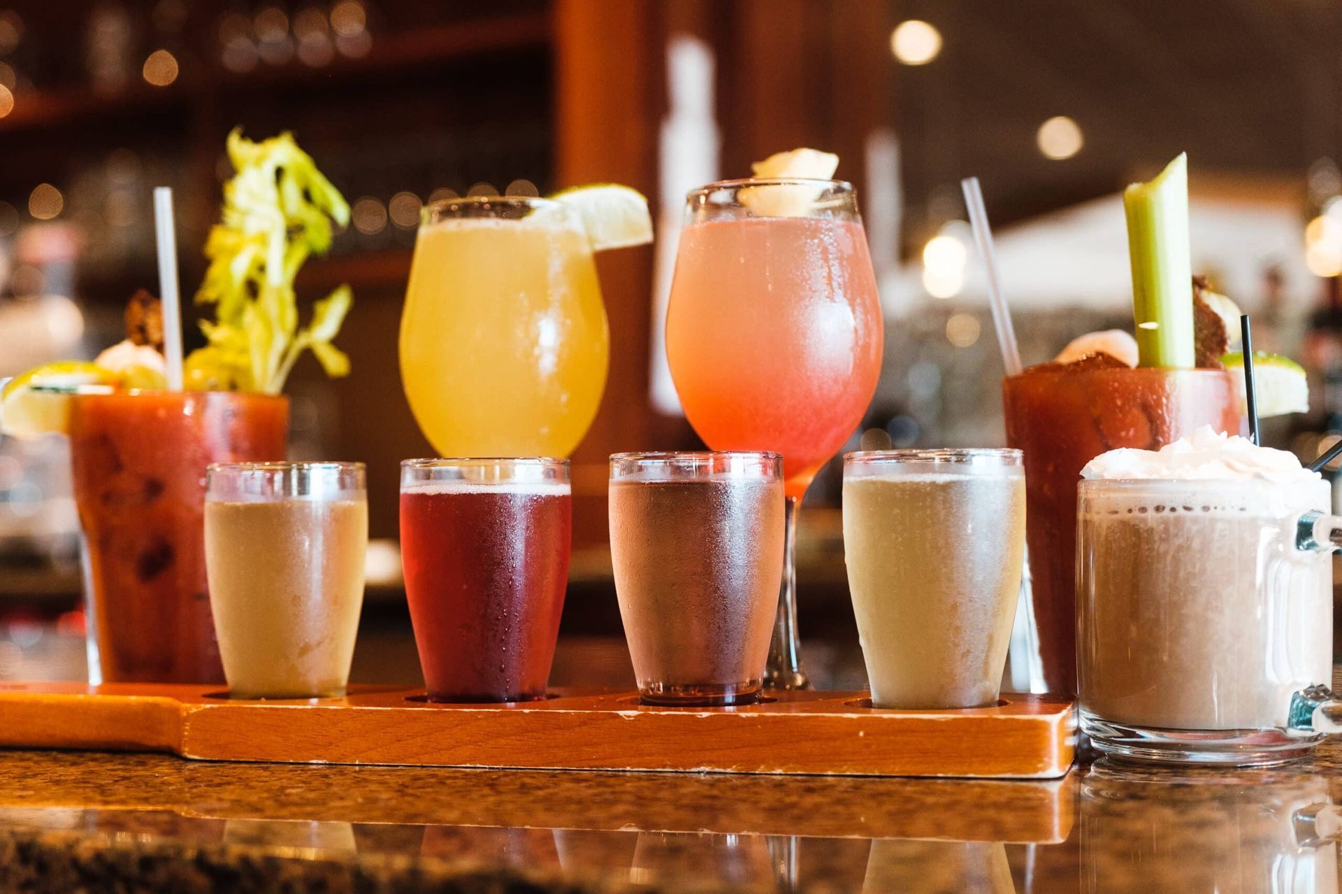 A variety of drinks are sitting on a wooden tray on a bar.