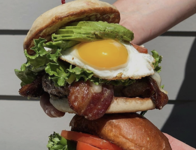 A person is holding a hamburger with eggs bacon and lettuce