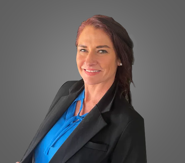 A woman in a blue shirt and black jacket is smiling for the camera.