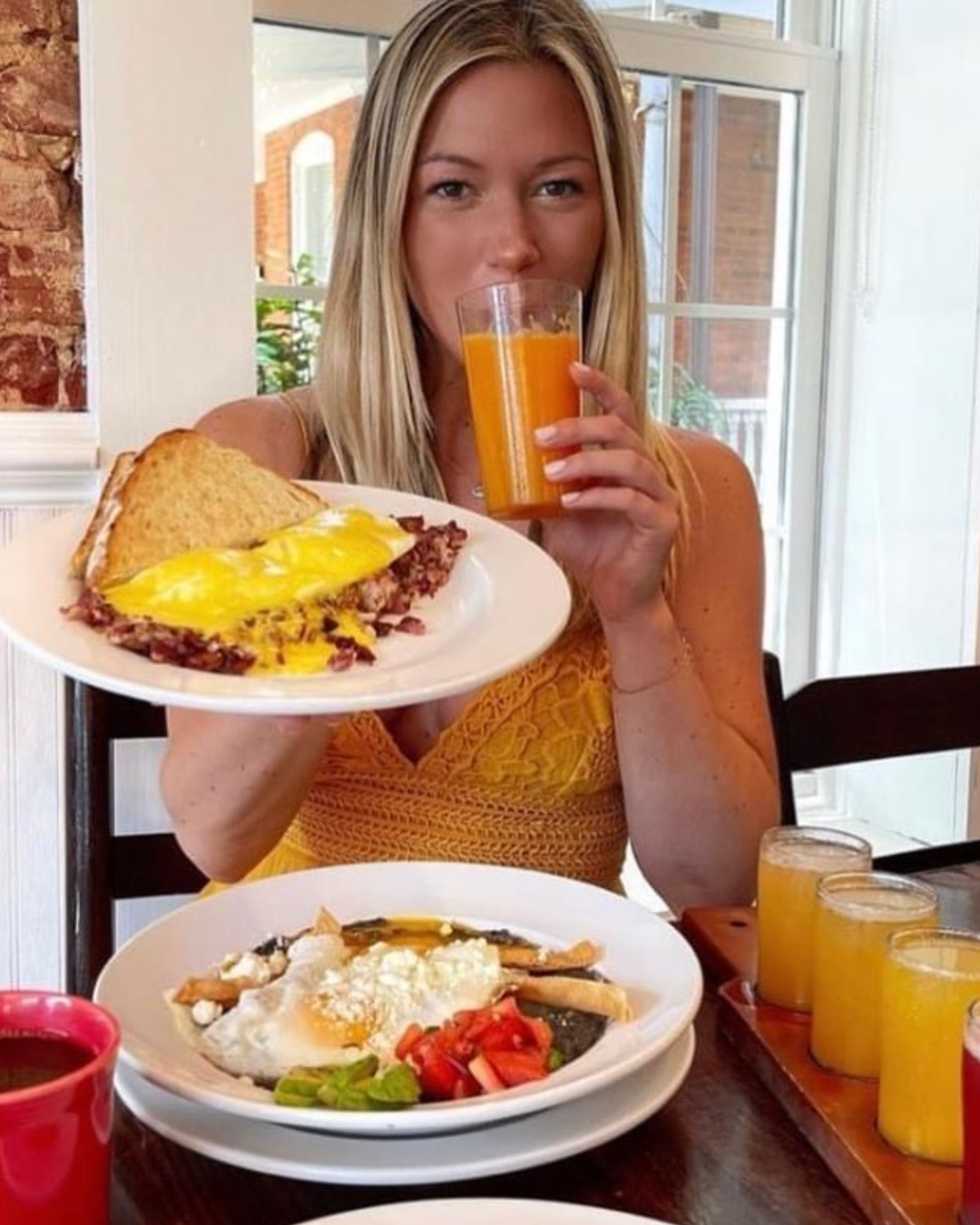 A woman is holding a plate of food and drinking orange juice