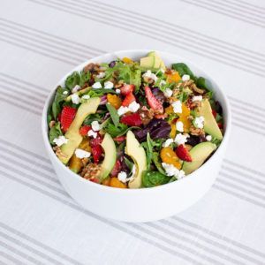 A white bowl filled with a salad with strawberries and avocado