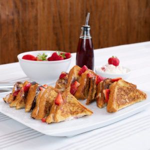 French toast with strawberries and syrup on a white plate