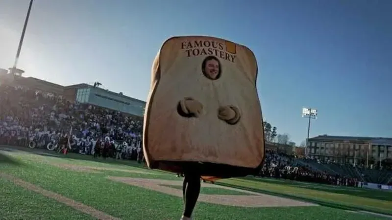 A person in a famous toastery costume is walking on a football field.