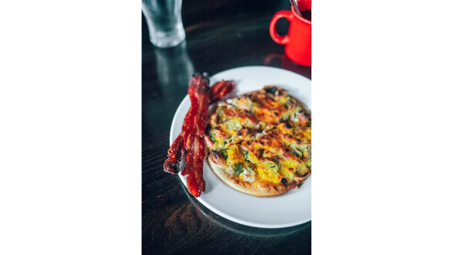 A white plate topped with a pizza and bacon on a table.