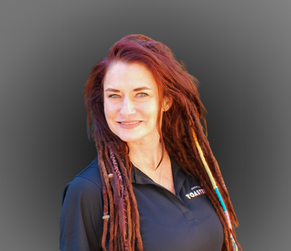 A woman in a blue shirt and black jacket is smiling for the camera.