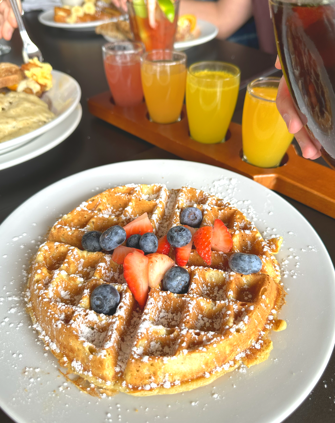 A waffle with strawberries and blueberries on a white plate