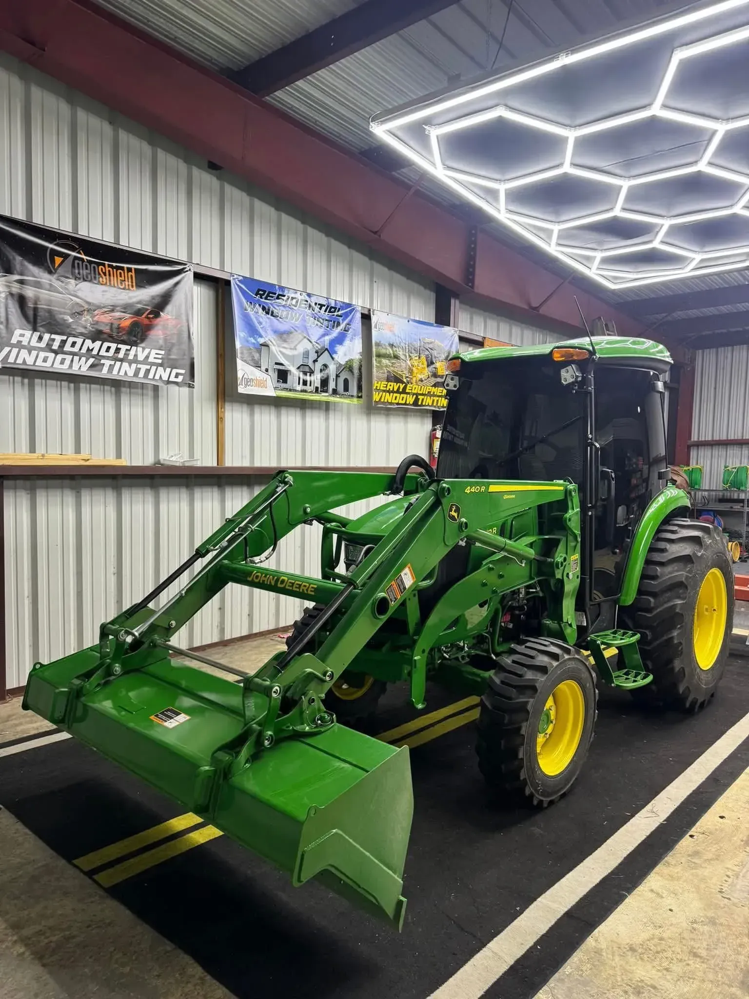 Green John Deere tractor with front loader inside a garage with banners.