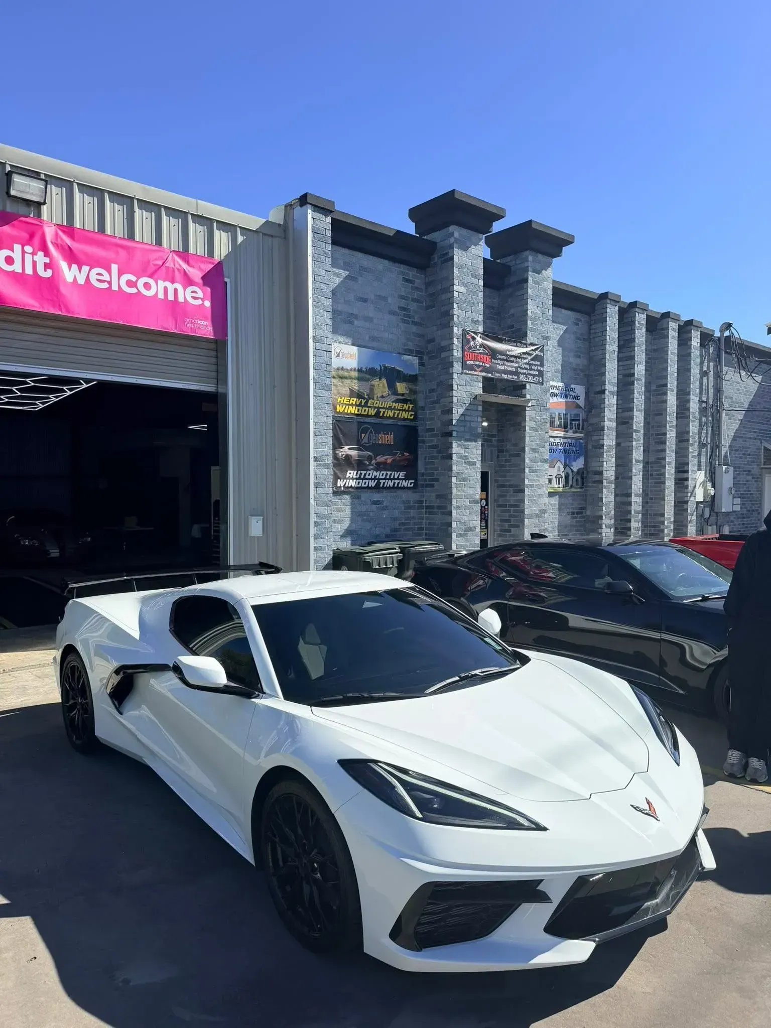 White sports car parked in front of a building with a pink banner that reads 