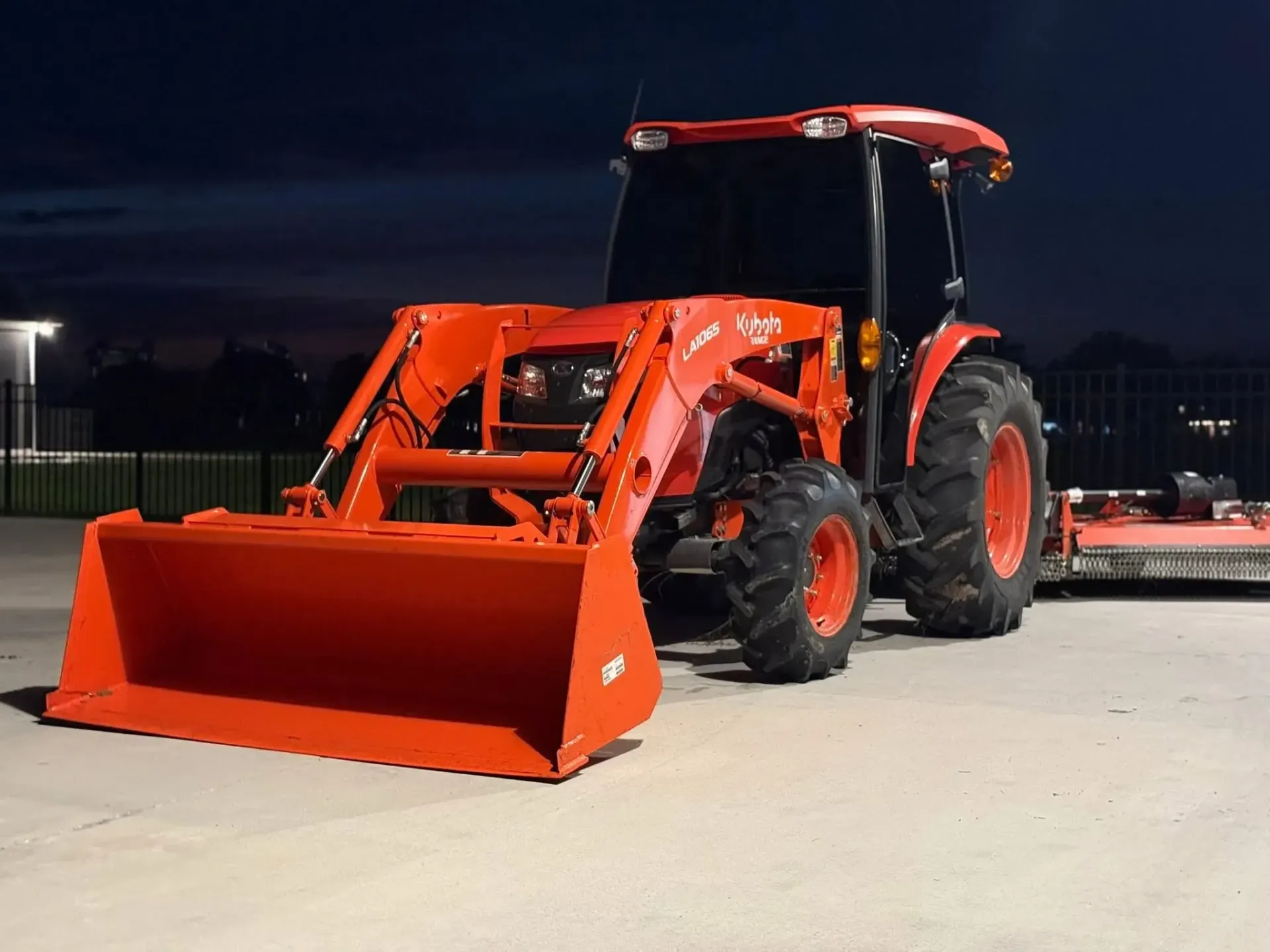 Orange tractor with front loader parked outdoors at dusk.