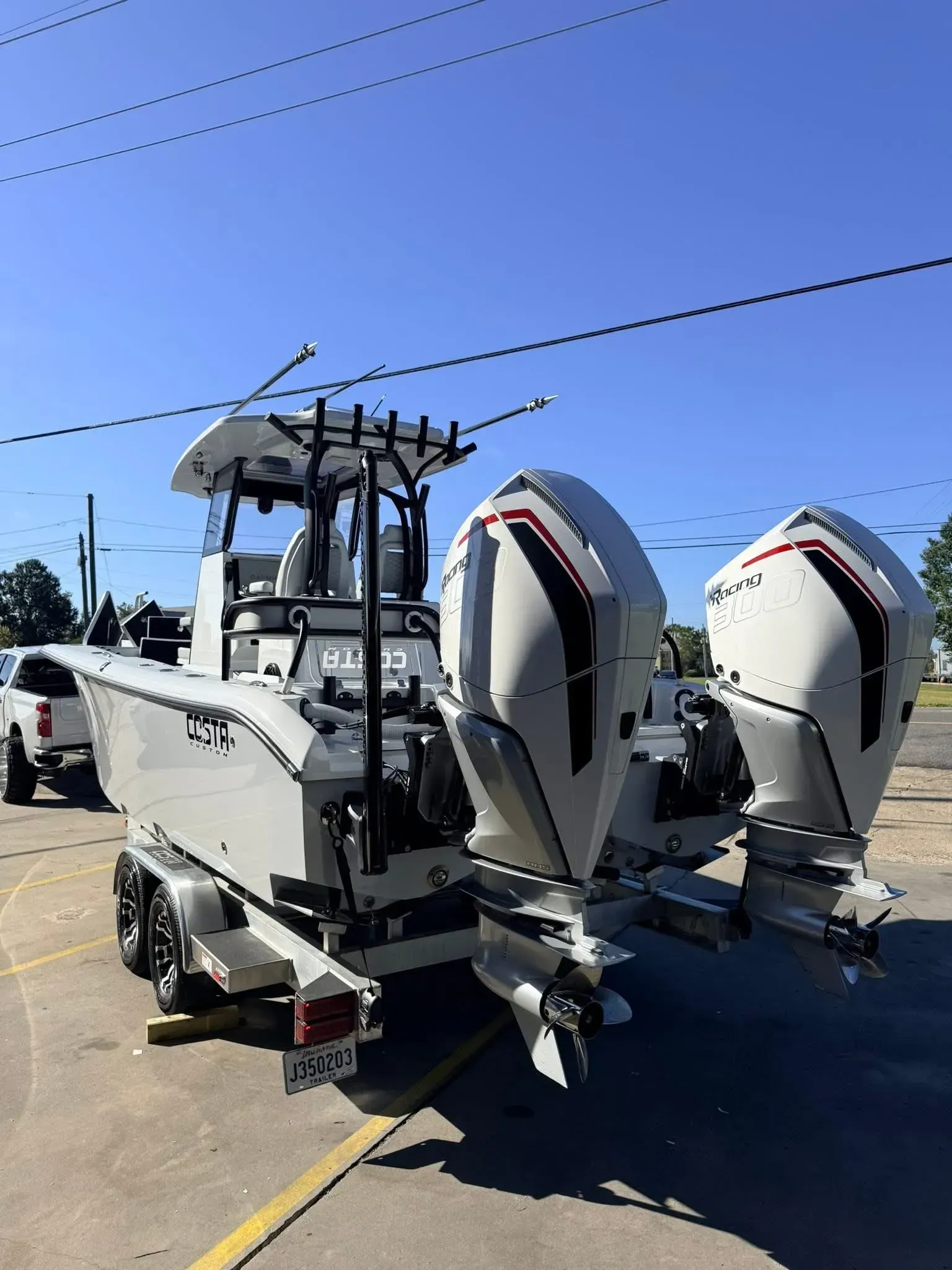 A white boat with two large outboard motors on a trailer in an outdoor setting under a blue sky.