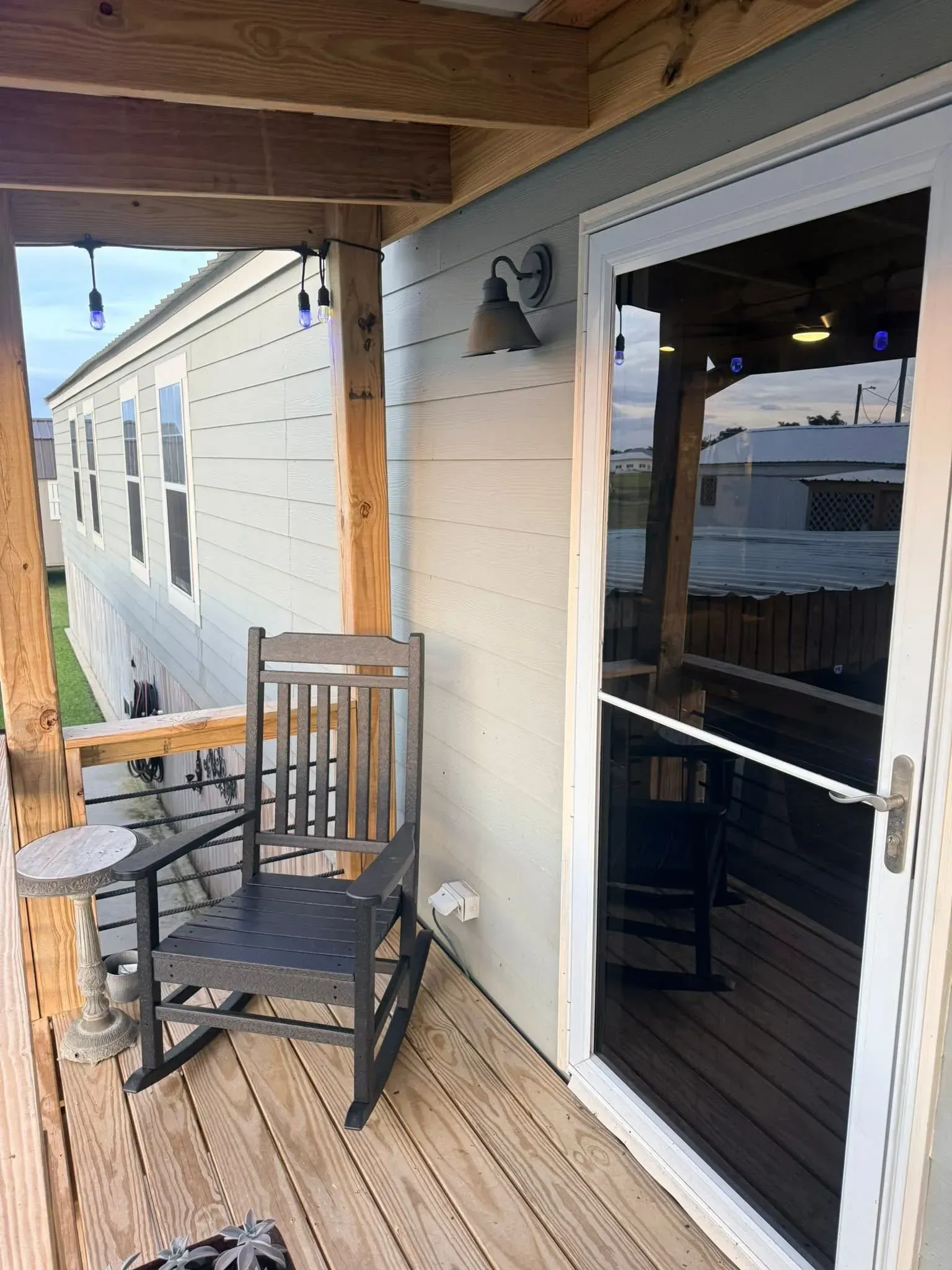 A small porch with a rocking chair, small table, and a sliding glass door.