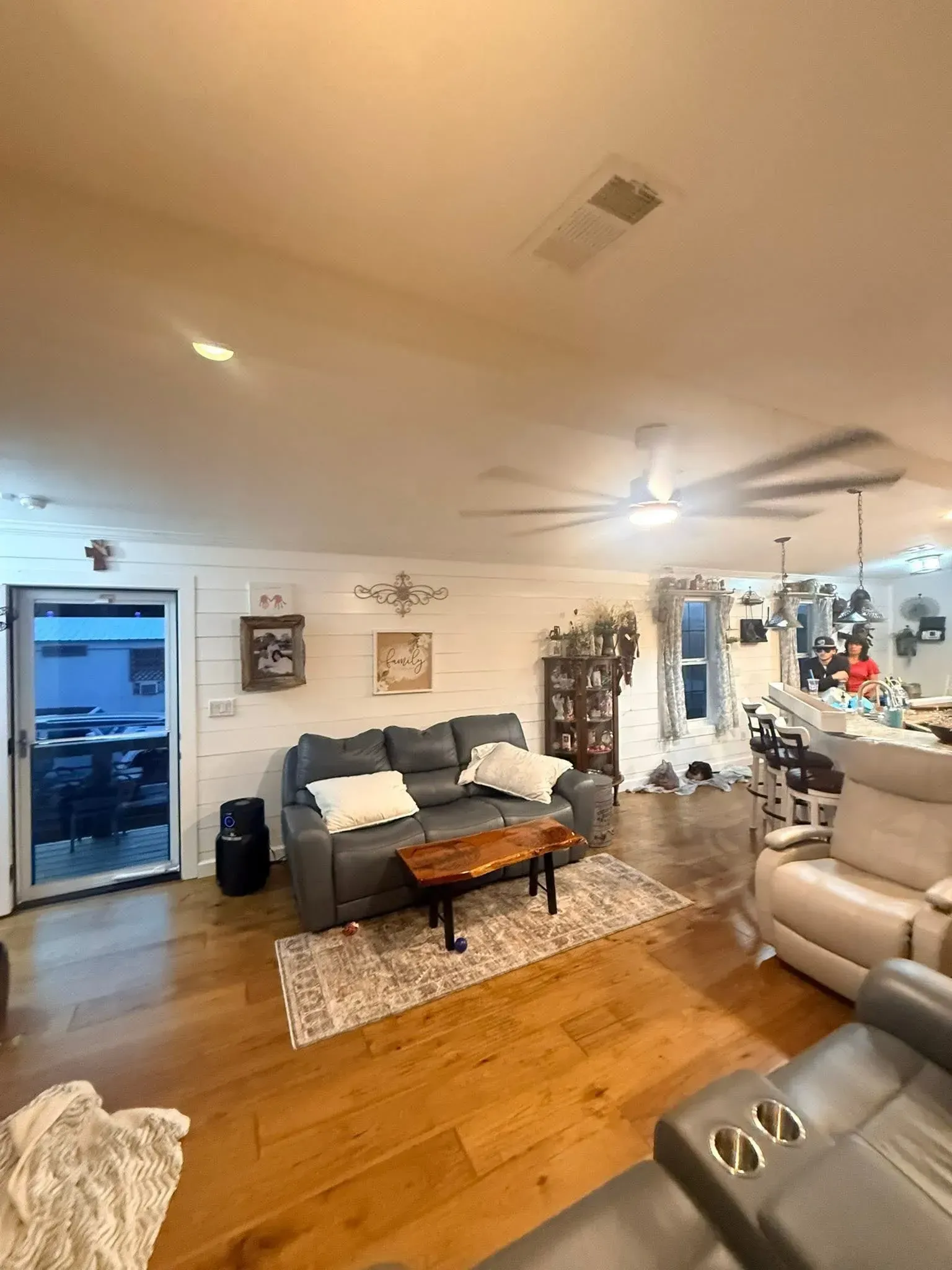 Open living space with hardwood floors, a gray leather sofa, and a kitchen area with a bar.