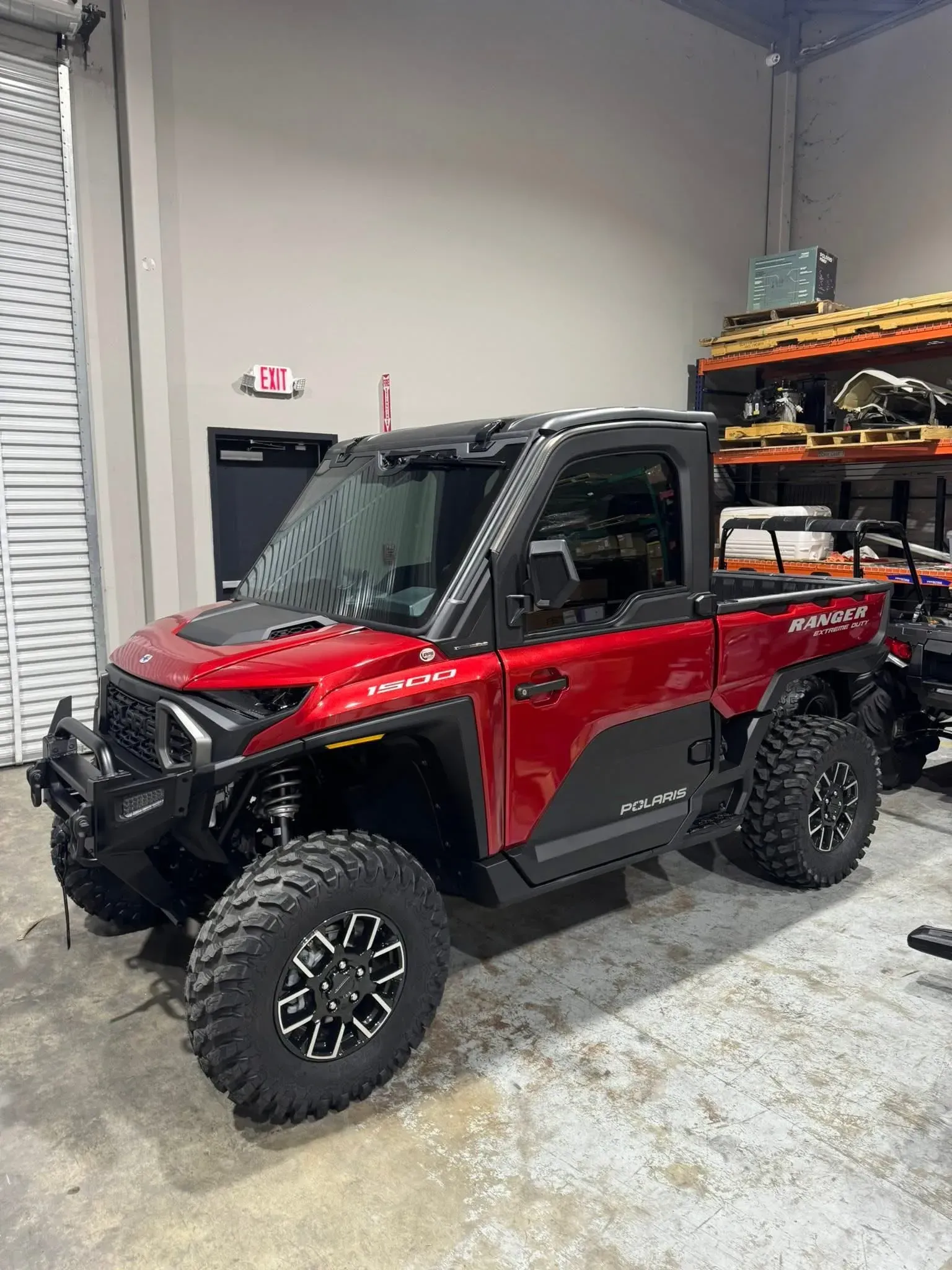 Red and black utility terrain vehicle (UTV) with large tires, parked inside a warehouse.