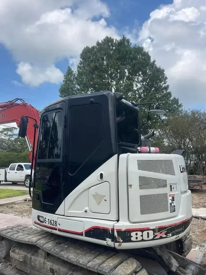 White and black Link-Belt 80X excavator on a construction site with a cloudy sky backdrop.
