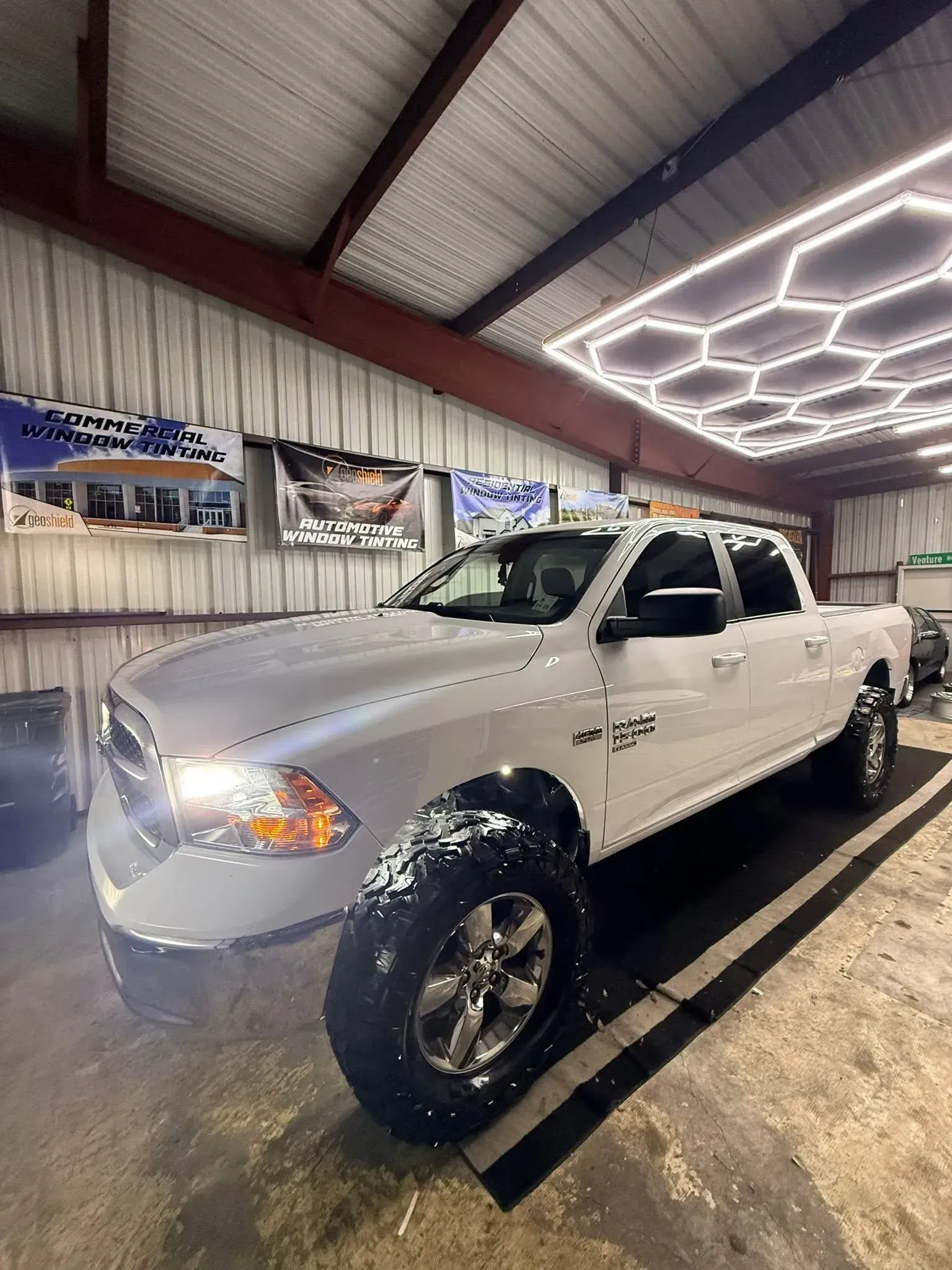 White lifted Ram pickup truck inside a garage with bright hexagon lights overhead.