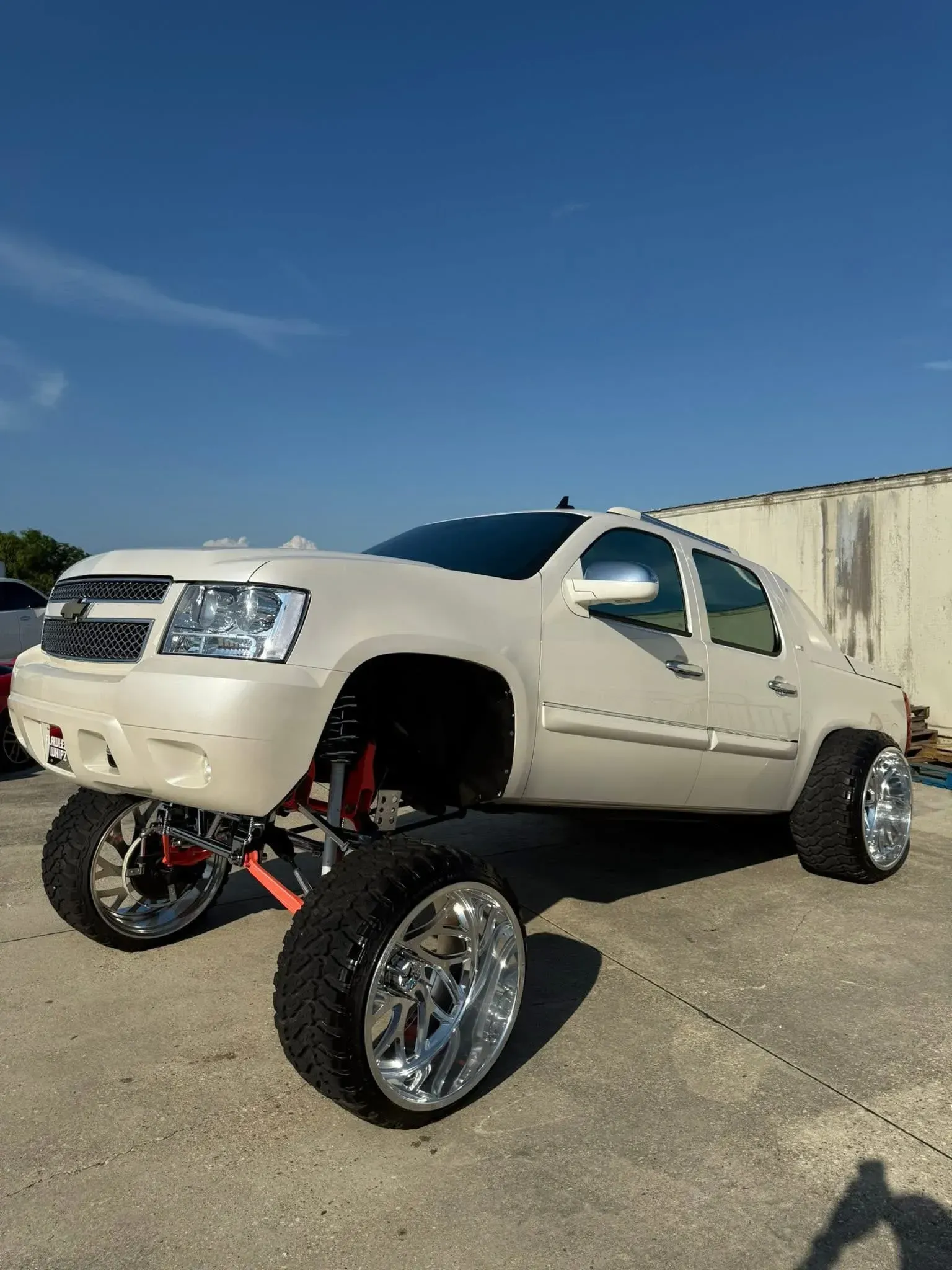 White lifted Chevy Avalanche truck with large chrome wheels and tires.