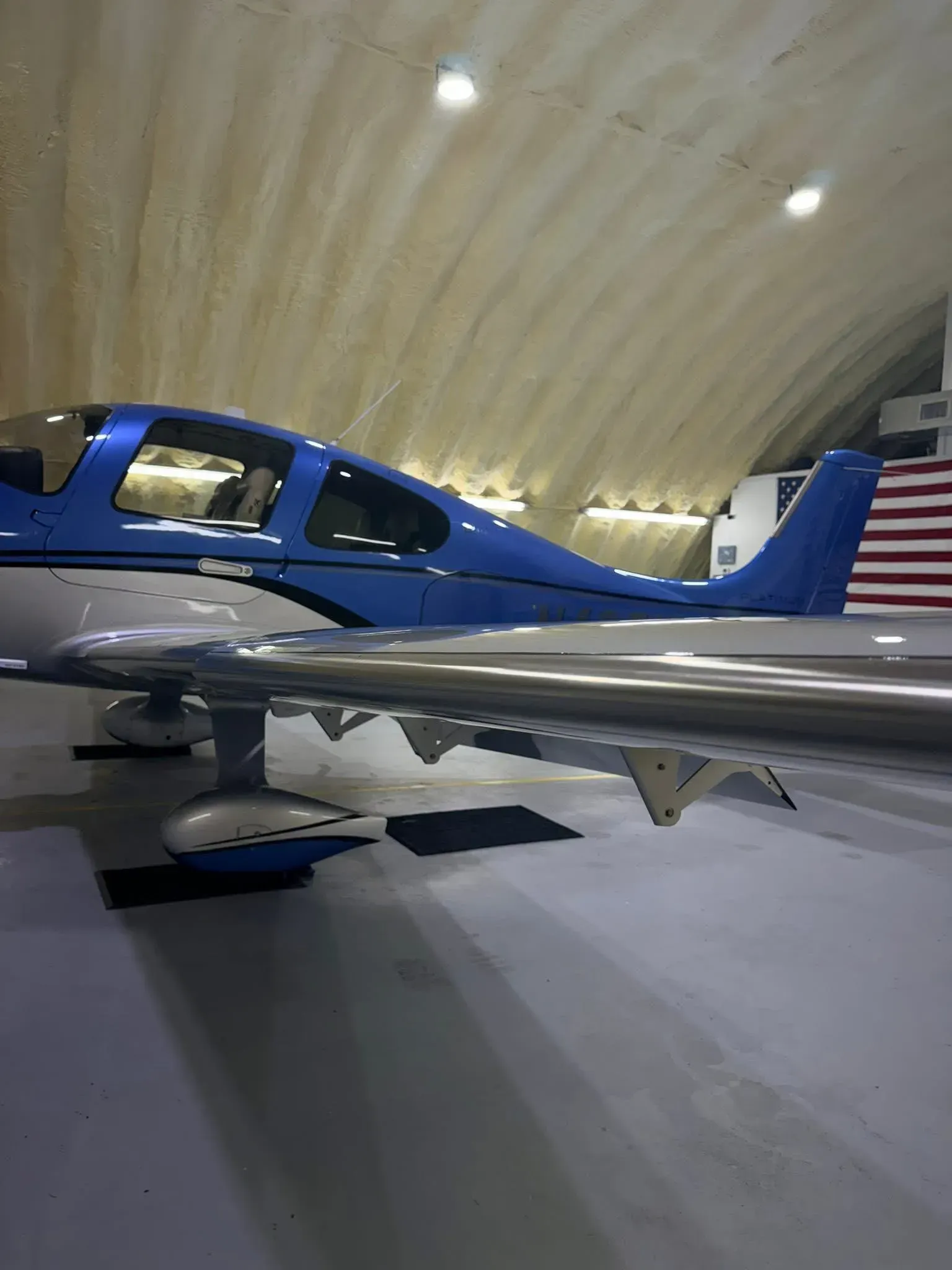 Blue and silver airplane parked inside a hangar; the US flag is visible in the background.
