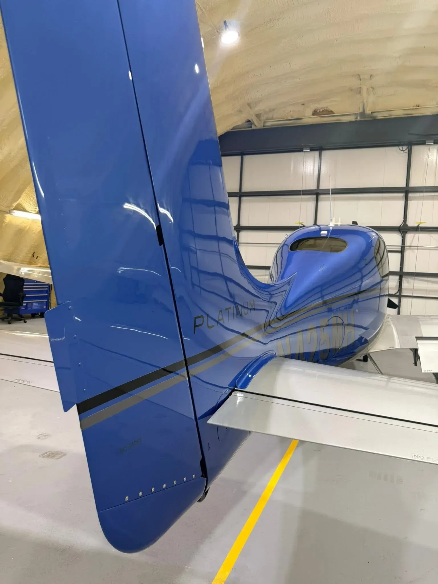 Blue airplane tail and fuselage in a hangar, wing visible.