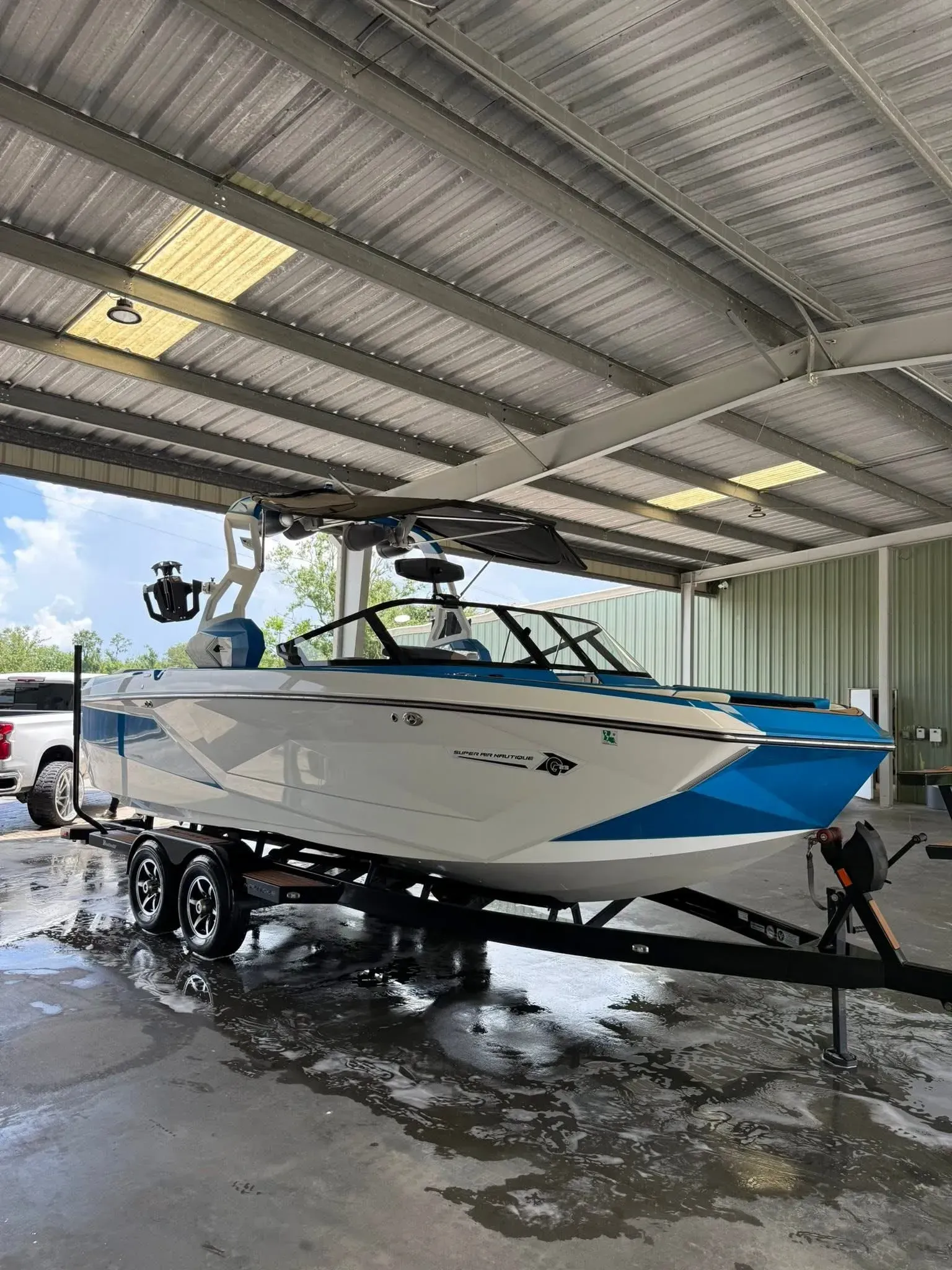 White and blue motorboat on a trailer under a metal roof, with a black tower.