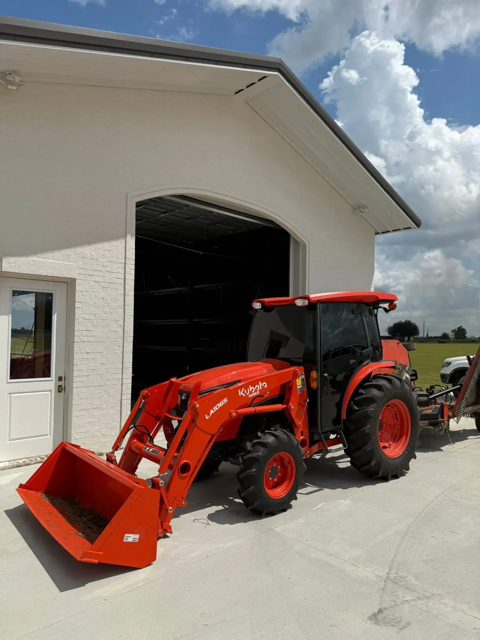 Red tractor with a front loader parked in front of a white building with an open bay door.